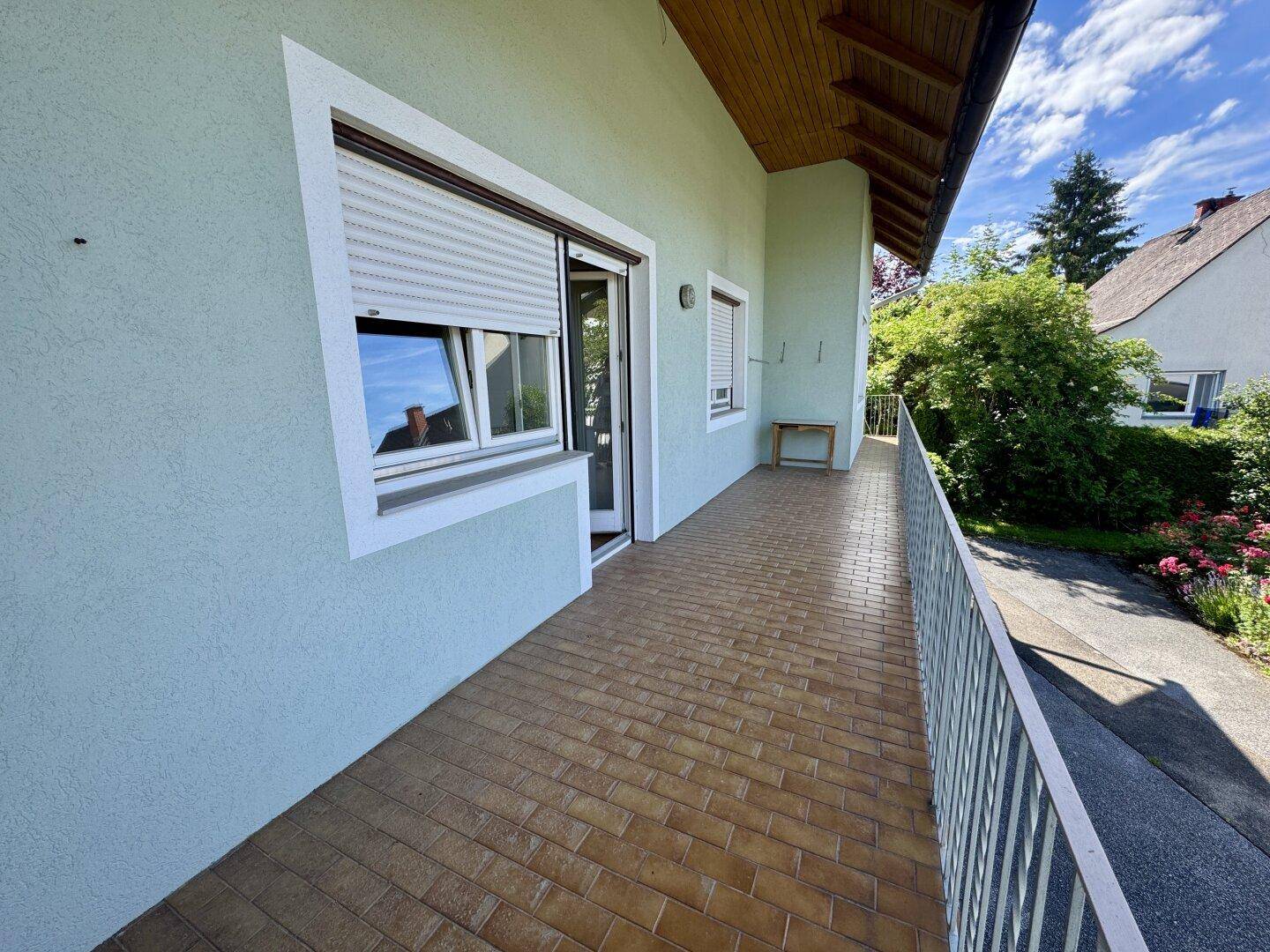 Langer Balkon mit Fliesenboden, Metallgeländer und Rollläden, bietet einen grünen Ausblick.