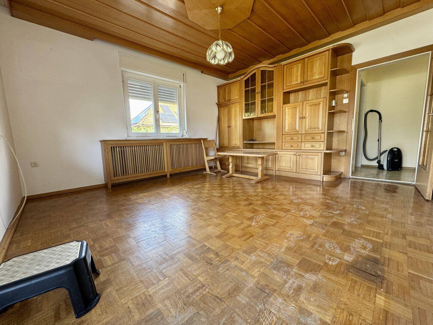 Geräumiges Wohnzimmer mit Holzdecke, Parkettboden und traditionellen Einbaumöbeln.