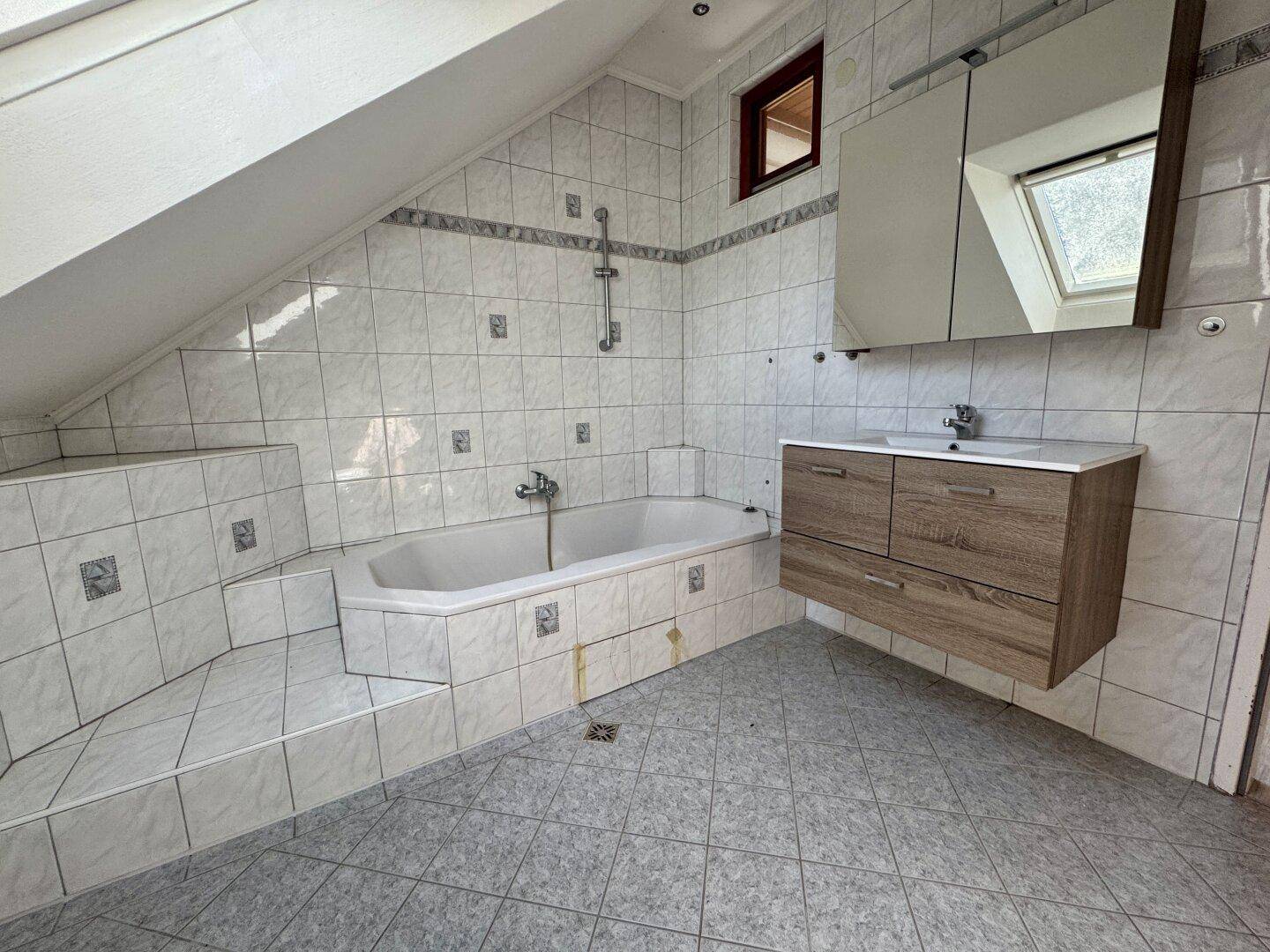 Helles Dachgeschoss-Badezimmer mit Badewanne, Waschbecken und Spiegelschrank.