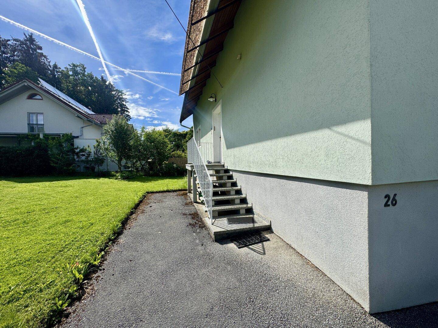 Seitenansicht des Hauses mit grünem Rasen und Außentreppe.