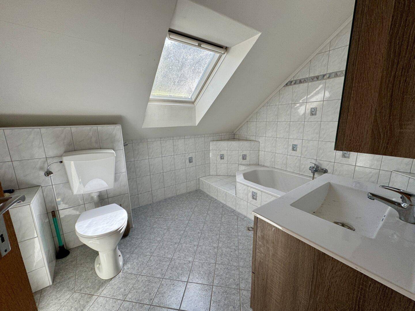 Dachgeschoss-Badezimmer mit Badewanne, Dachfenster und Fliesenboden unter der Dachschräge.