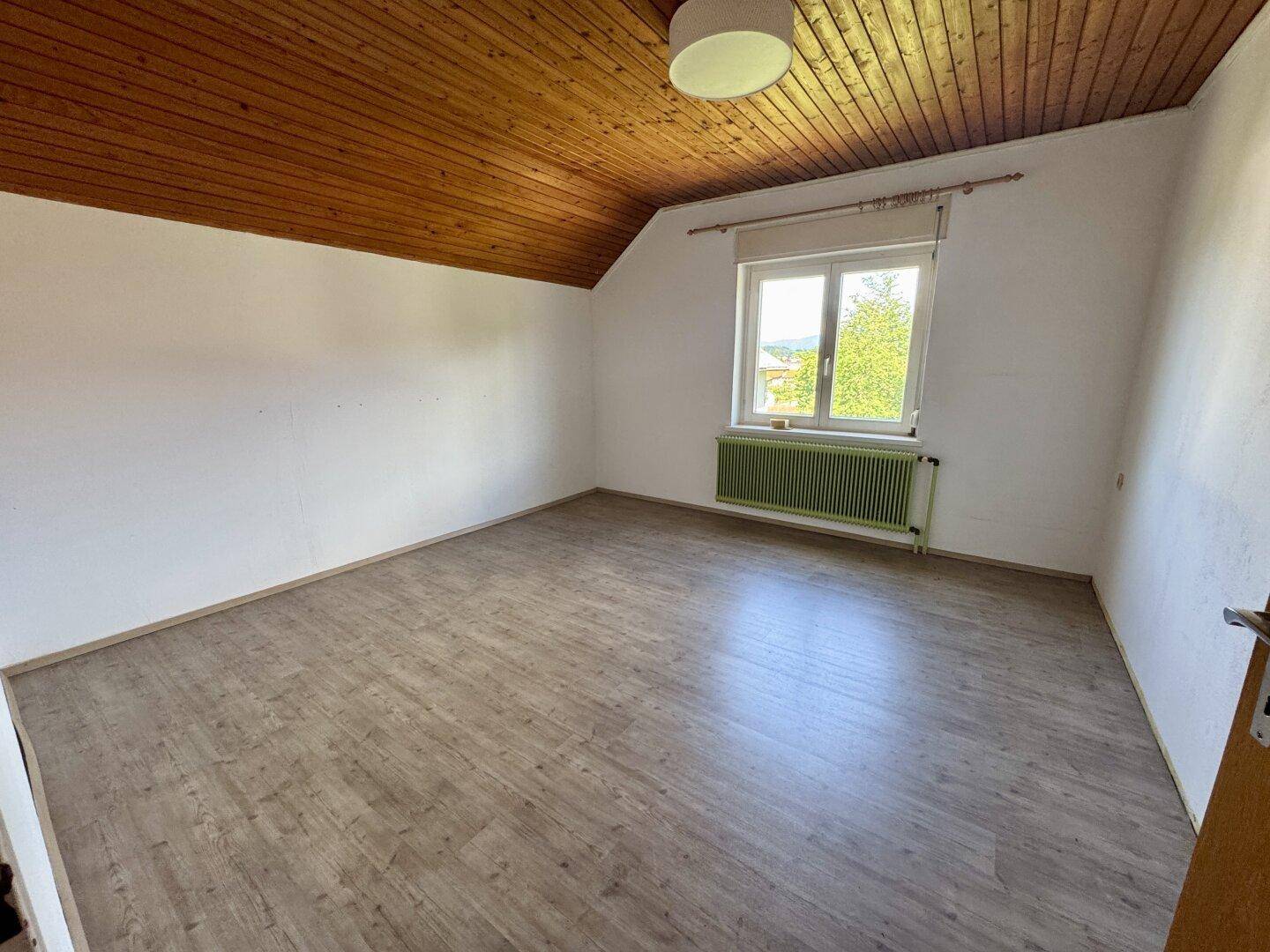 Helles Dachgeschosszimmer mit Holzbalkendecke, Laminatboden und Fenster.