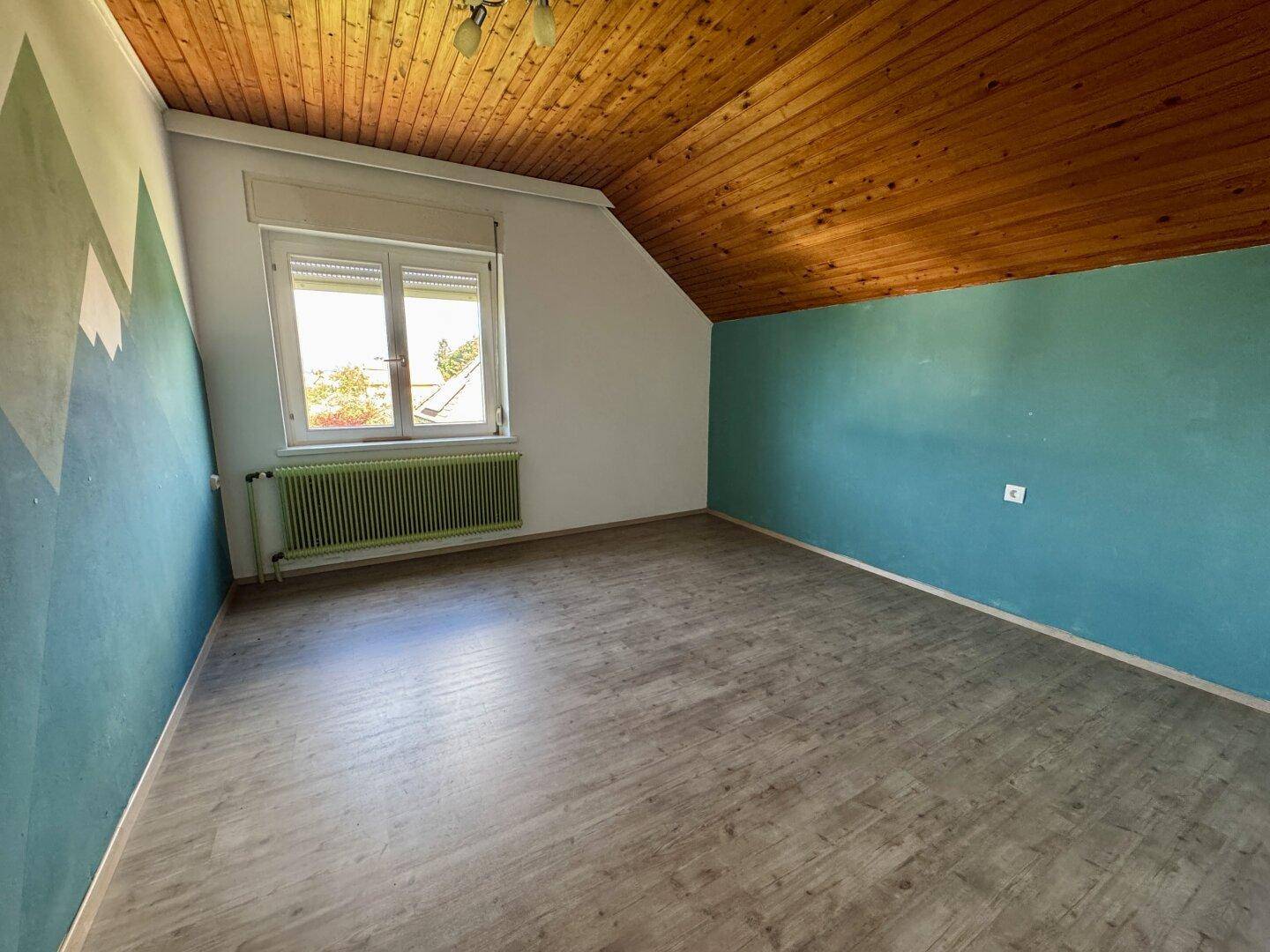 Dachgeschosszimmer mit Holzbalkendecke, Laminatboden und farbiger Wandgestaltung.