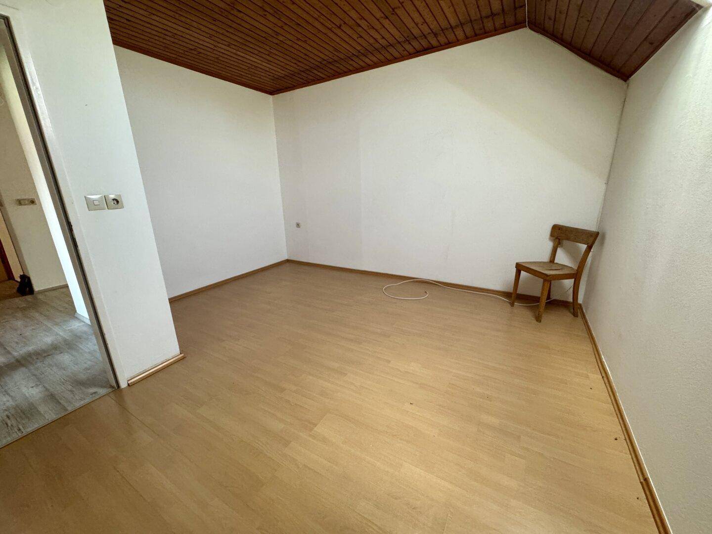 Leerer Raum mit Holzdecke, Laminatboden und einer einzelnen Holzstuhl.