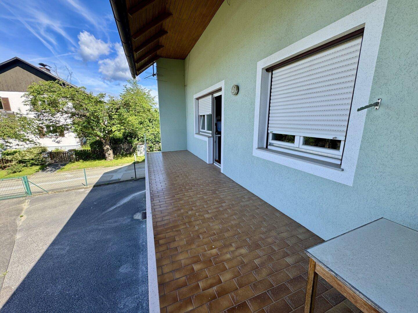 Überdachte Terrasse mit braunen Fliesen und Blick ins Grüne.