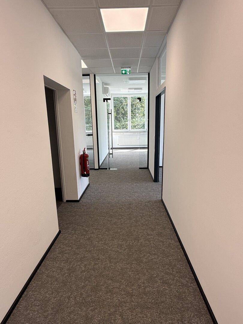 Langer Flur mit Teppichboden und Zugang zu mehreren Büroräumen, ausgestattet mit Brandschutz.