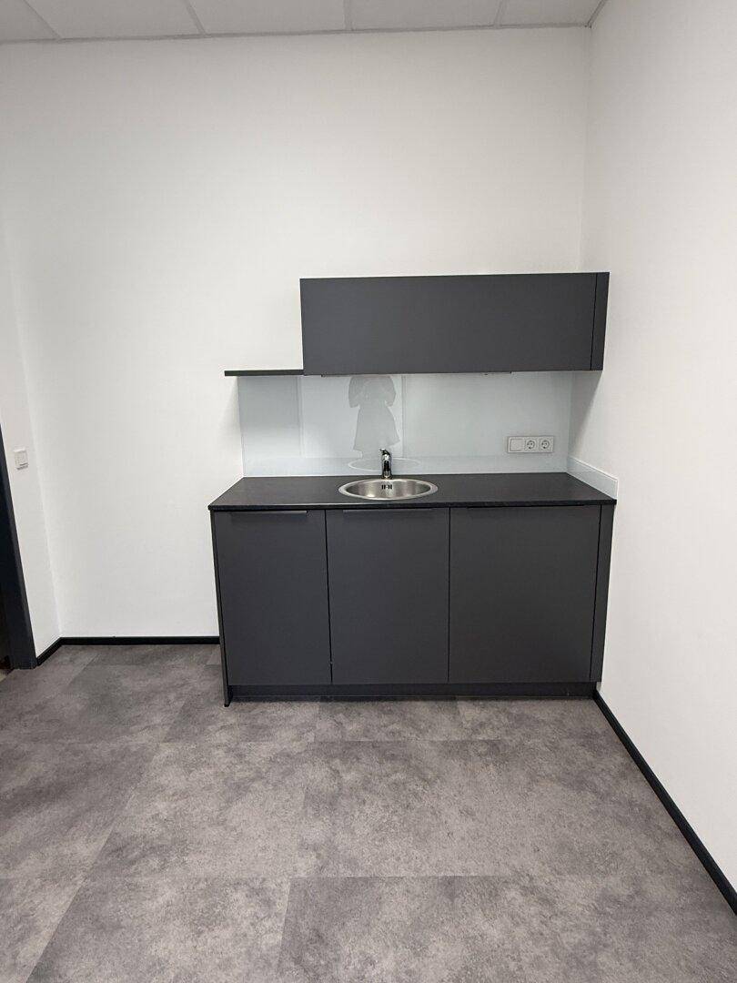 Moderne Küchenzeile in Grau mit Spülbecken und Stauraum, ideal für eine Büroküche.