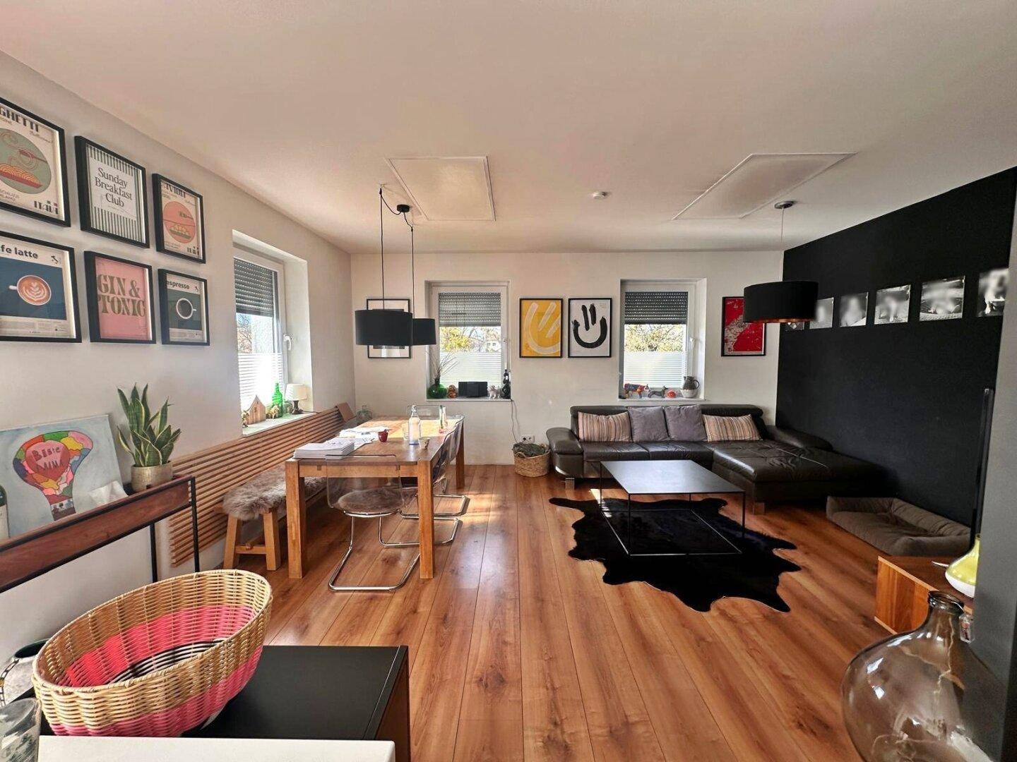 Geräumiger Wohn-Essbereich mit Holzboden, dunklem Sofa und moderner Dekoration.