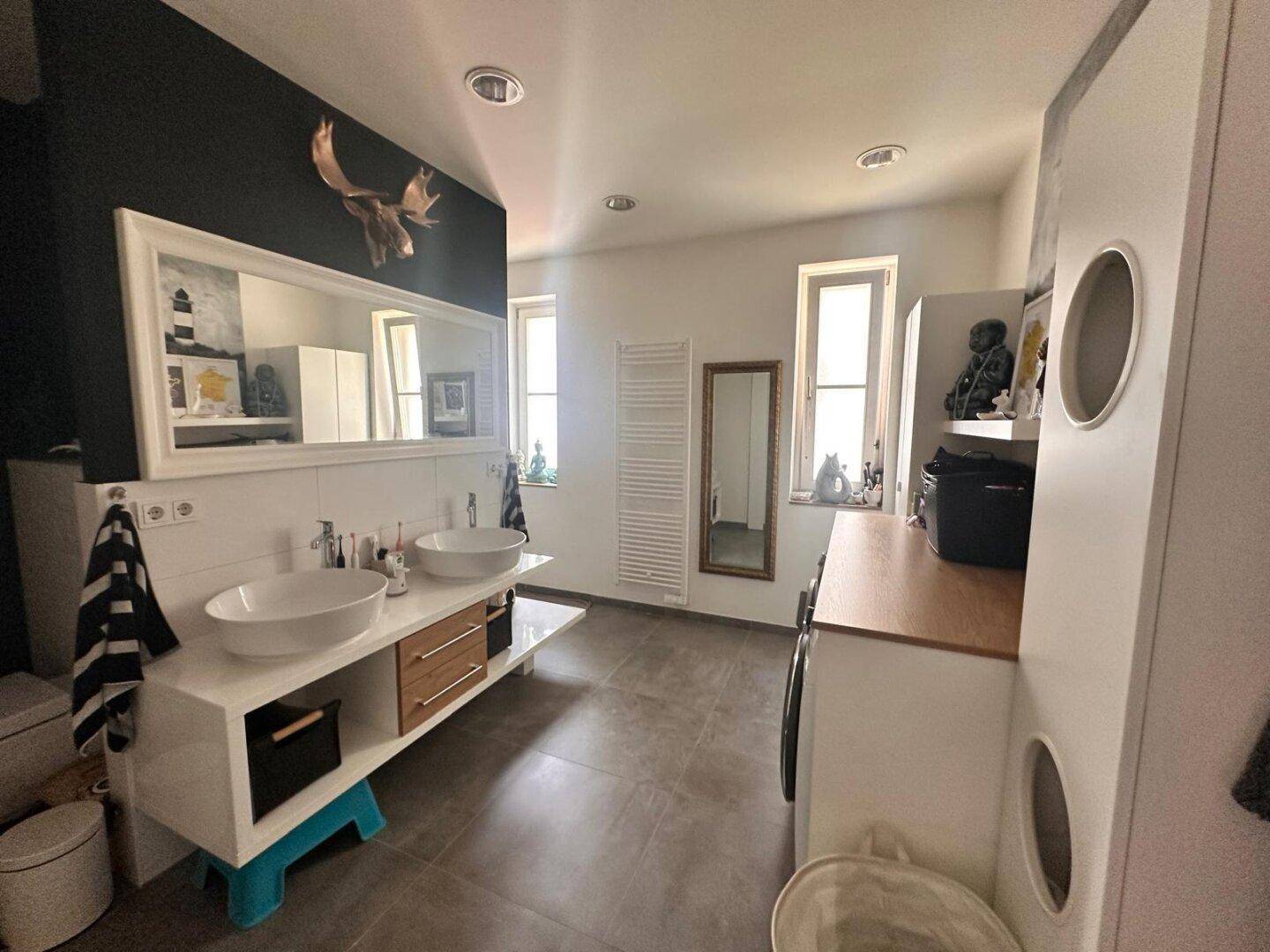 Modernes Badezimmer mit Doppelwaschbecken, großem Spiegel und dunklen Fliesen.