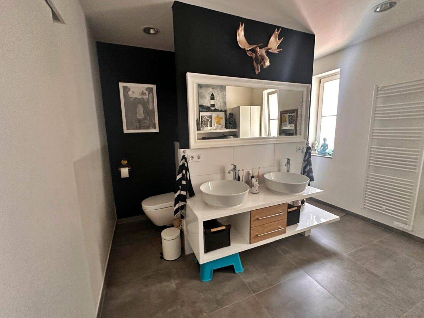 Stilvolles Badezimmer mit Doppelwaschbecken, Wand-WC und dunkler Akzentwand.