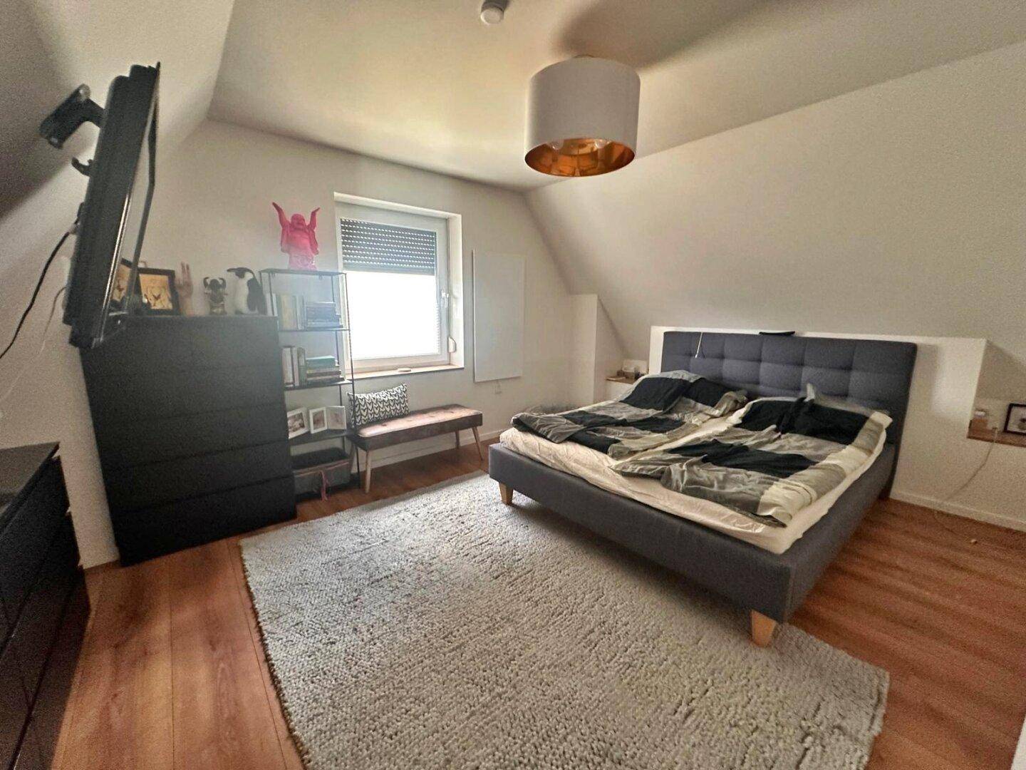 Gemütliches Schlafzimmer im Dachgeschoss mit Doppelbett, Teppich und Dachschräge.