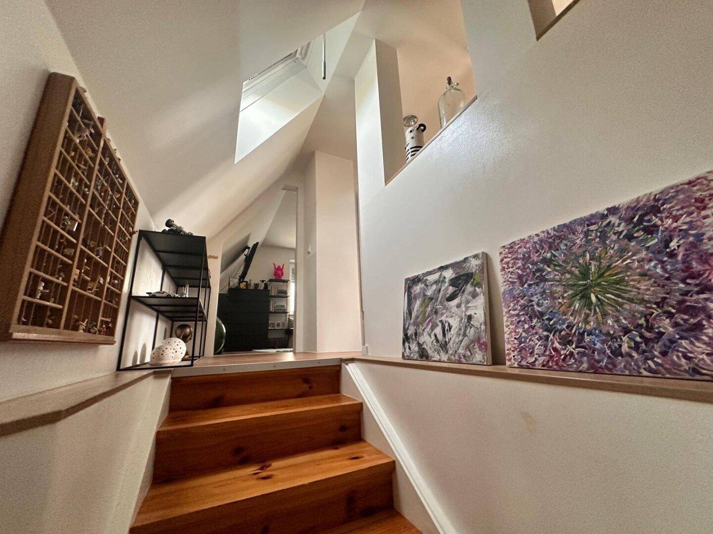 Holztreppe führt zu einem hellen Obergeschoss mit Kunstwerken an der Wand.