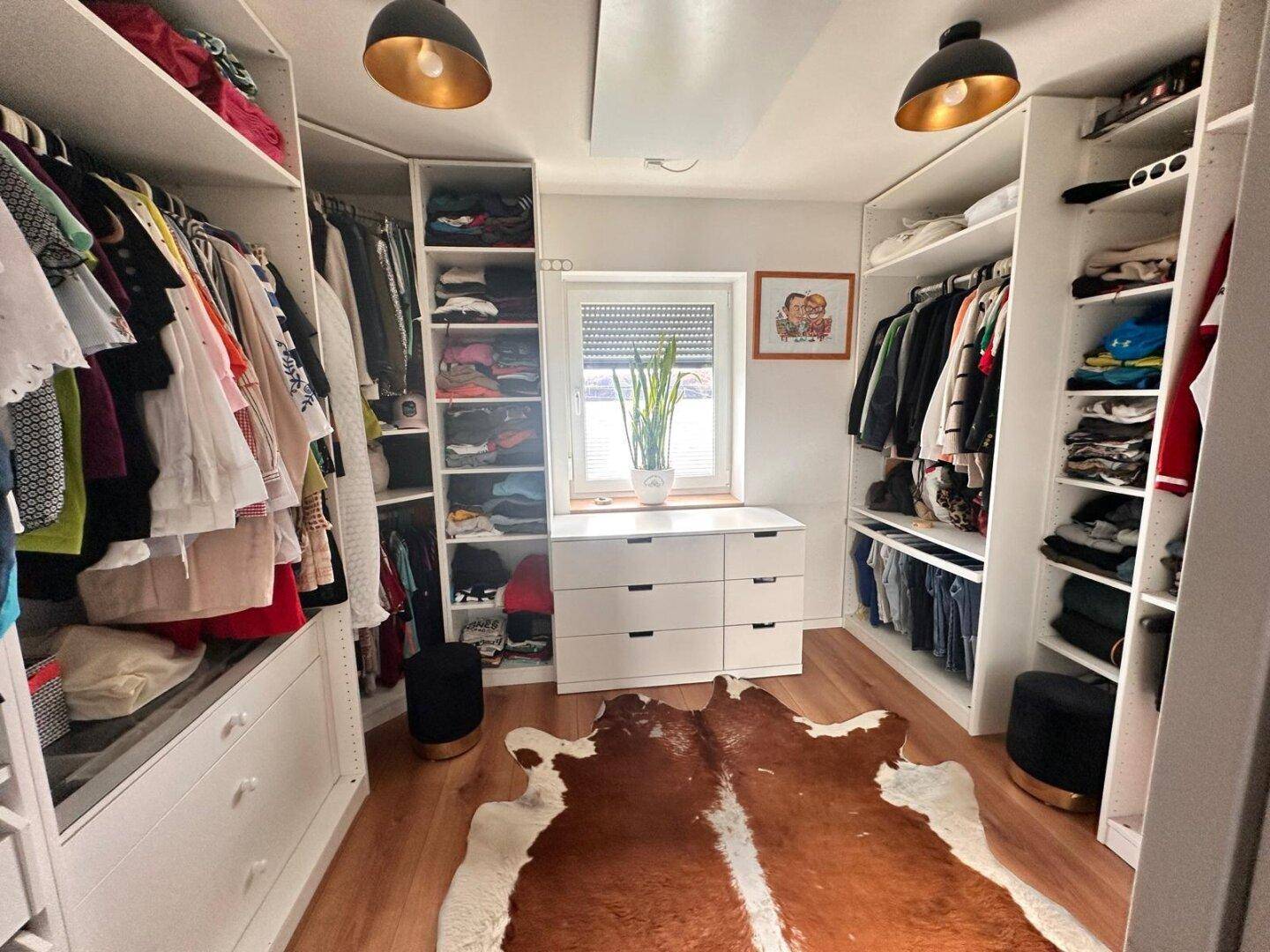 Geräumiger begehbarer Kleiderschrank mit viel Stauraum und Fenster.