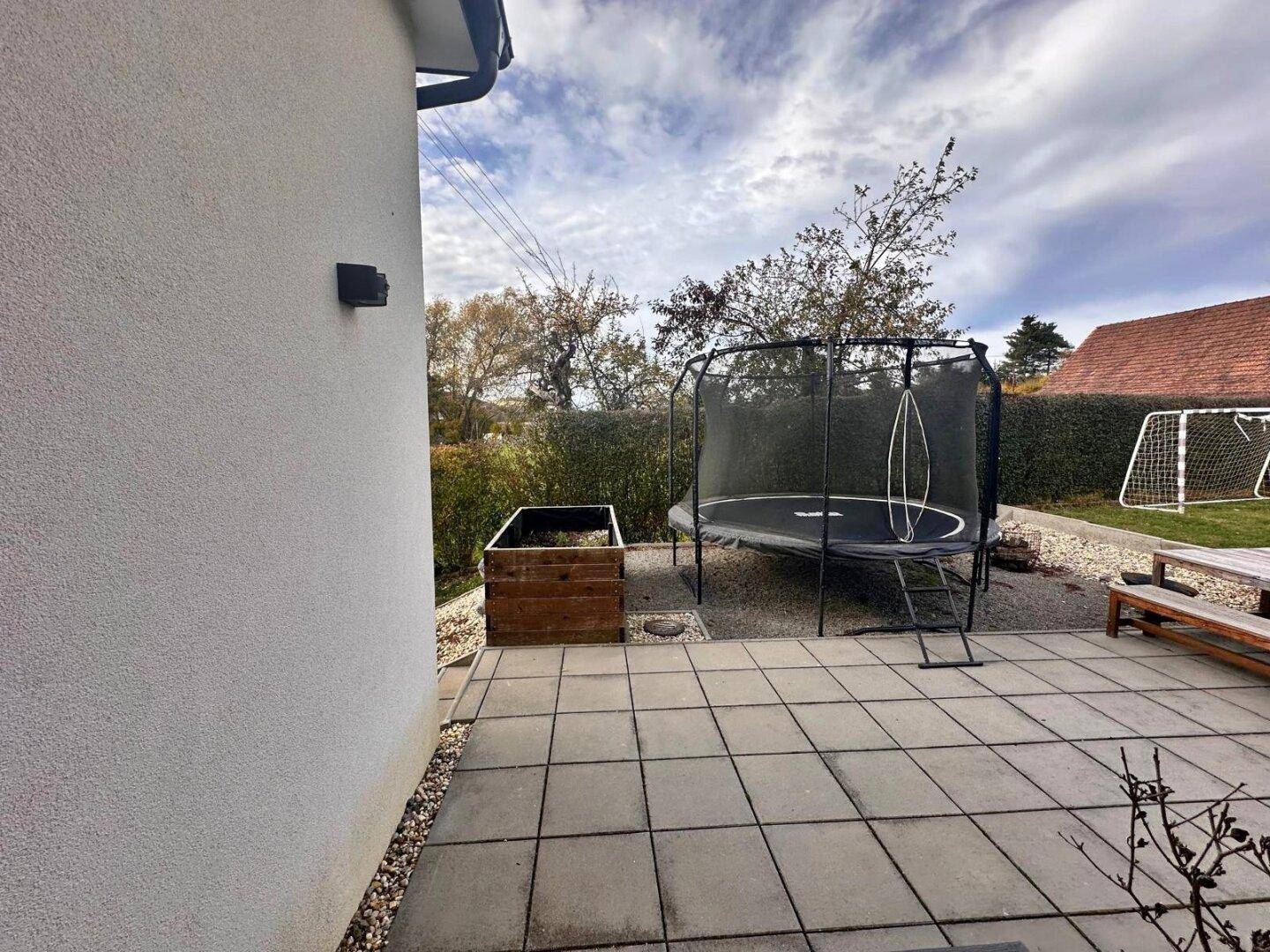 Gepflasterte Terrasse mit Trampolin und Blick auf den Garten.