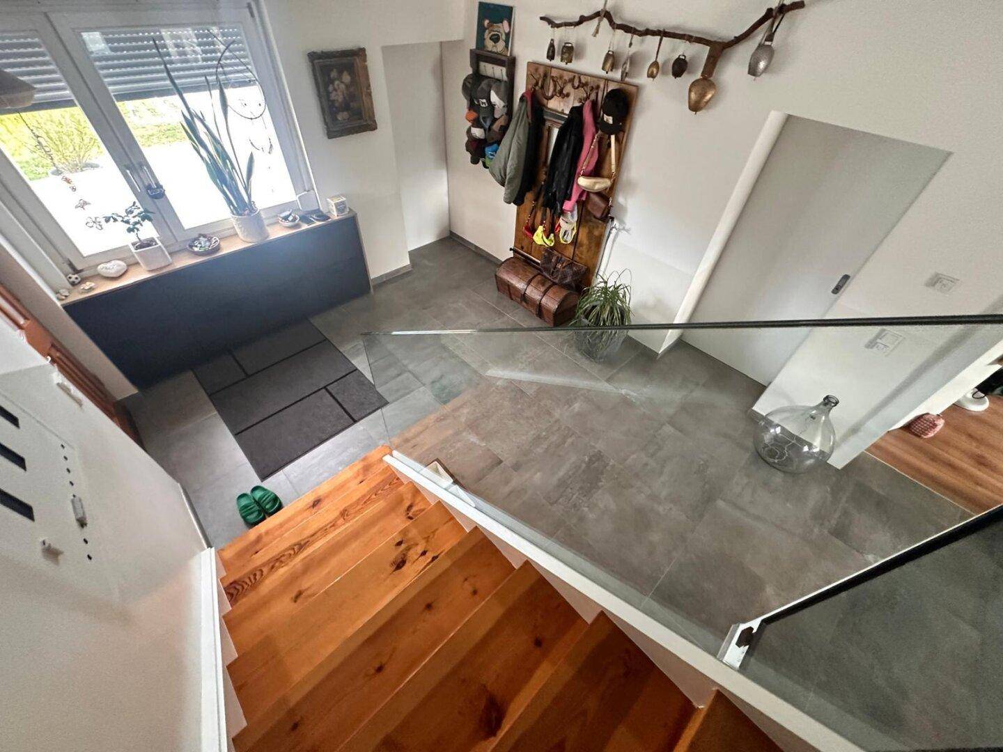 Eingangsbereich von oben gesehen mit Holztreppe und Fliesenboden.