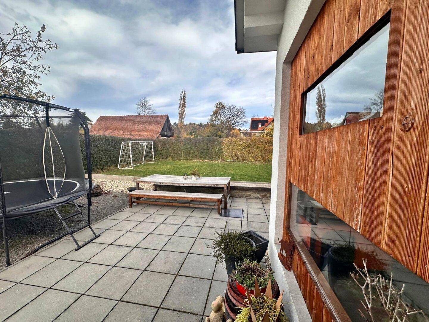 Gepflasterte Terrasse mit Holzelementen an der Fassade und Gartenblick.