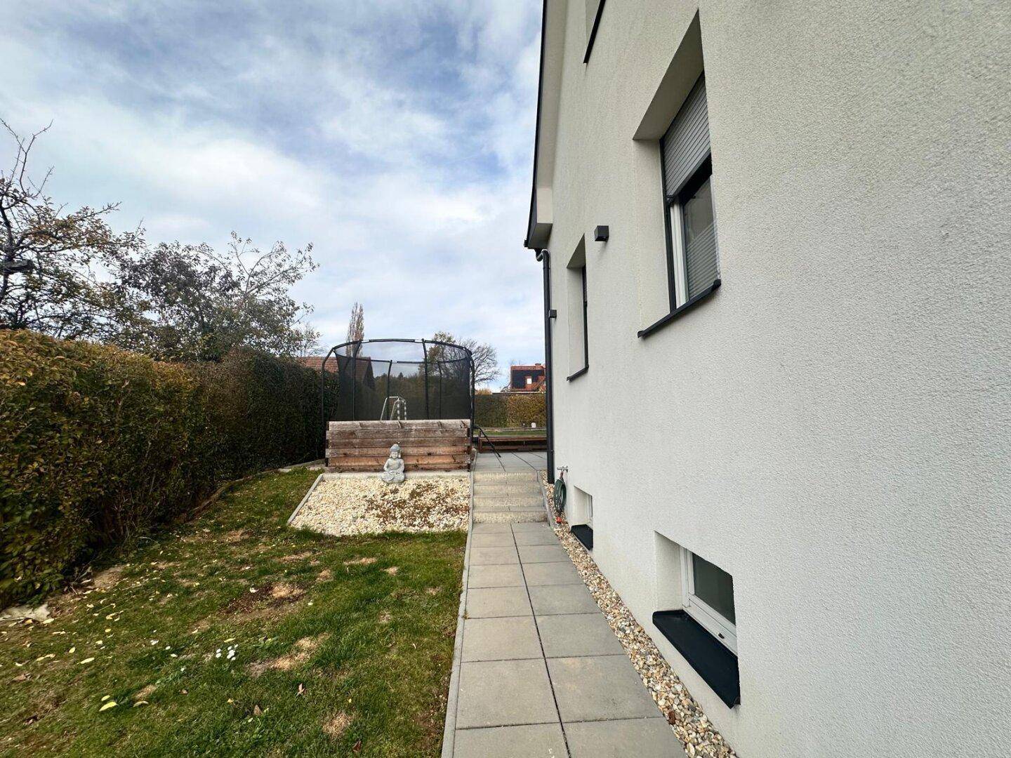 Seitenansicht des Hauses mit gepflastertem Weg und gepflegtem Gartenbereich.