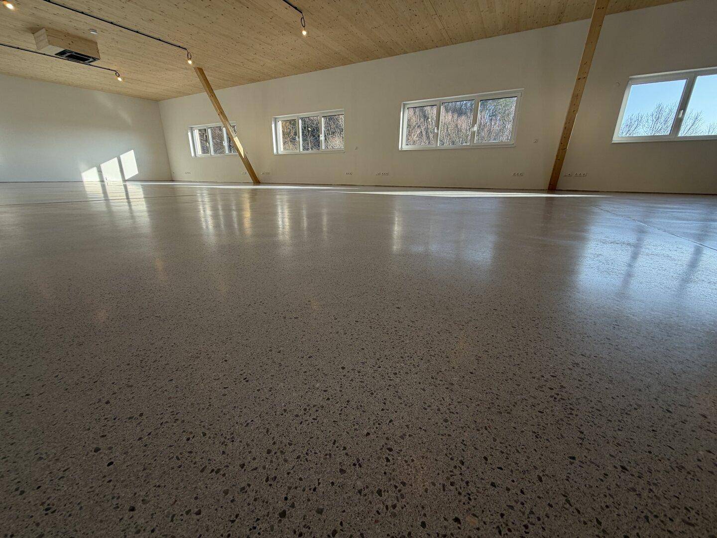 Nahaufnahme des glänzenden Betonbodens in einem großen, hellen Raum mit viel natürlichem Licht.