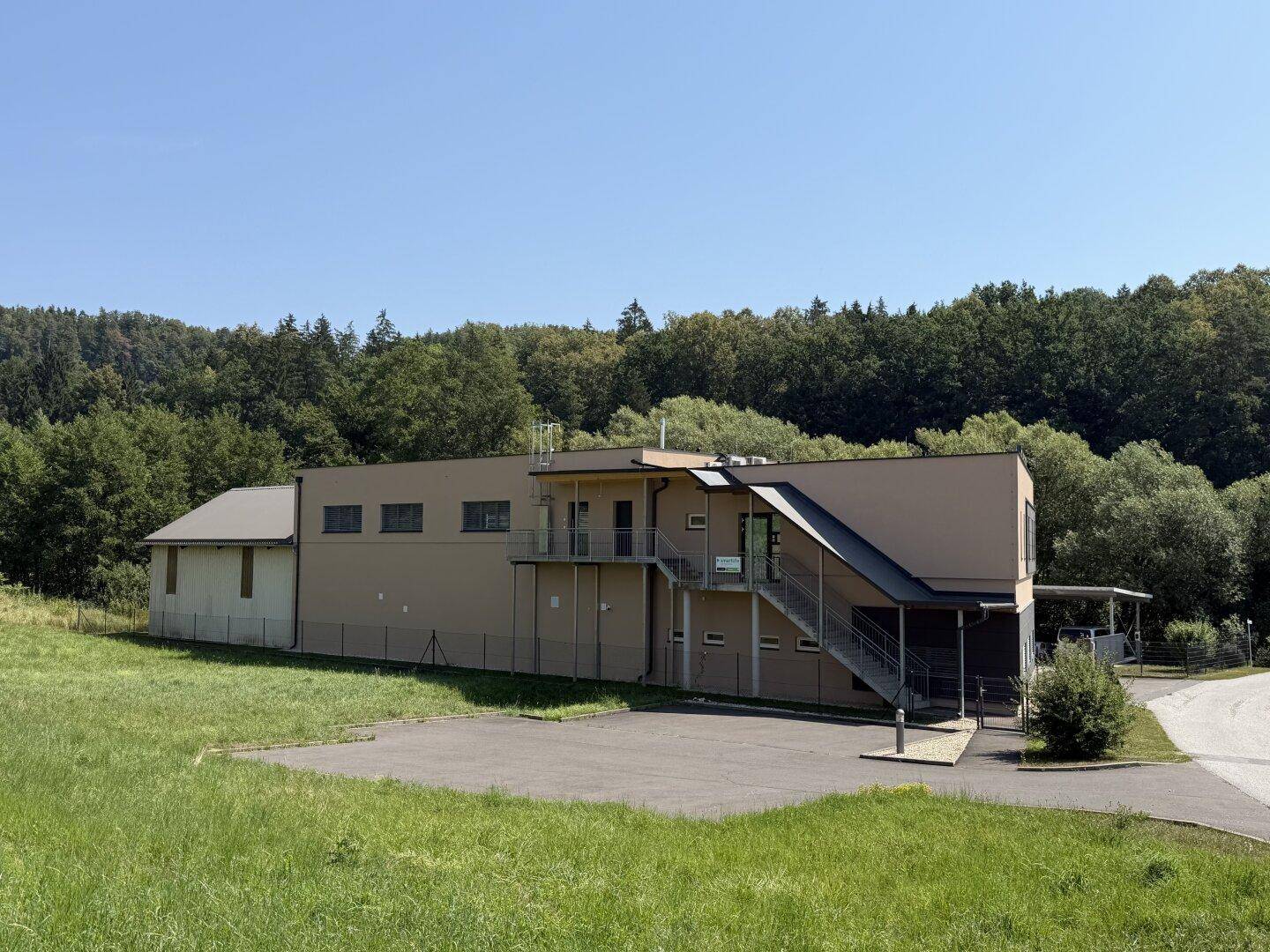 Rückansicht eines modernen Geschäftsgebäudes mit Außentreppe, umgeben von grünen Hügeln und Wald.