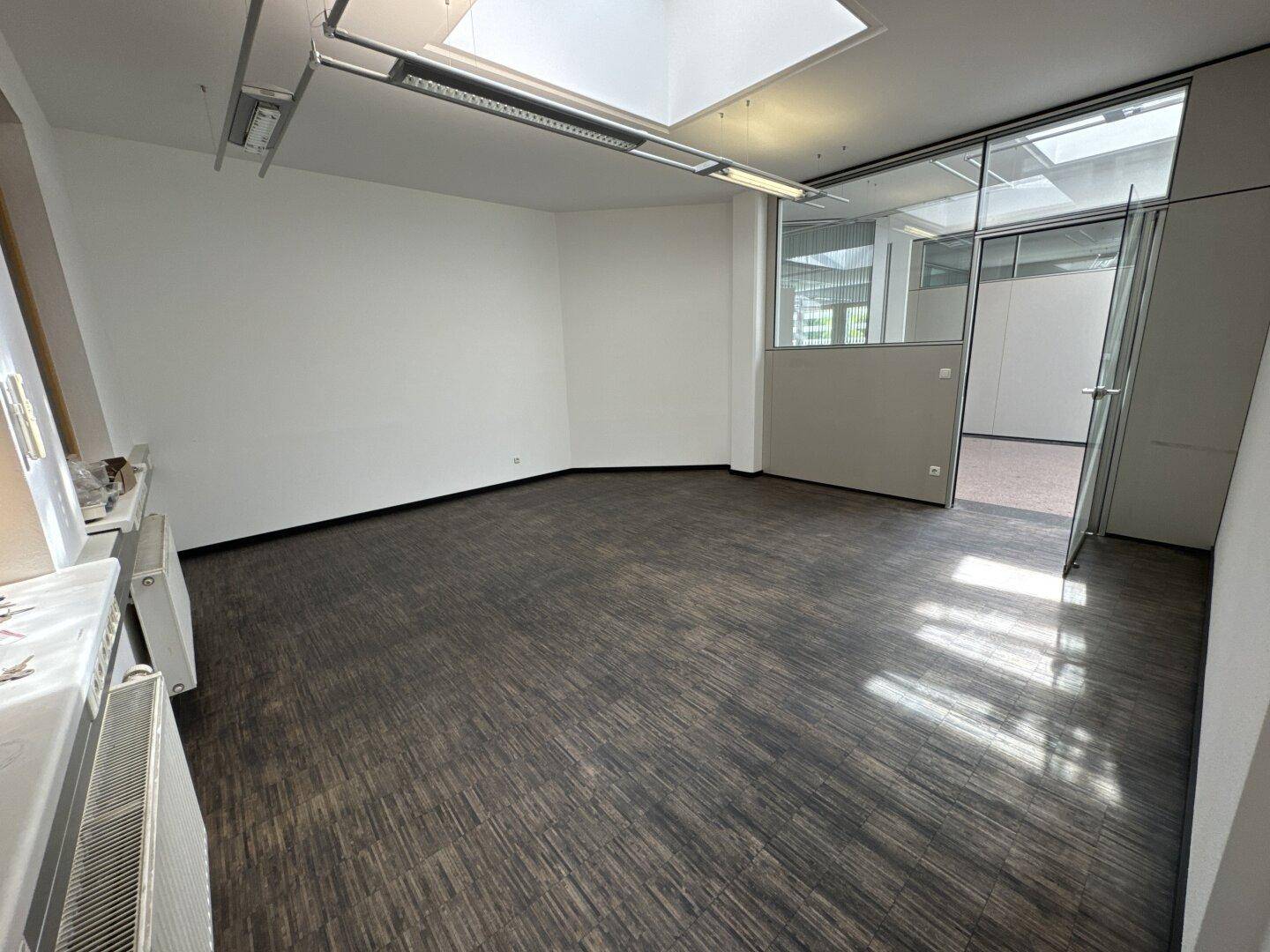 Leeres Büro mit dunklem Boden, Oberlicht und Glaswänden, die eine moderne Arbeitsumgebung schaffen.