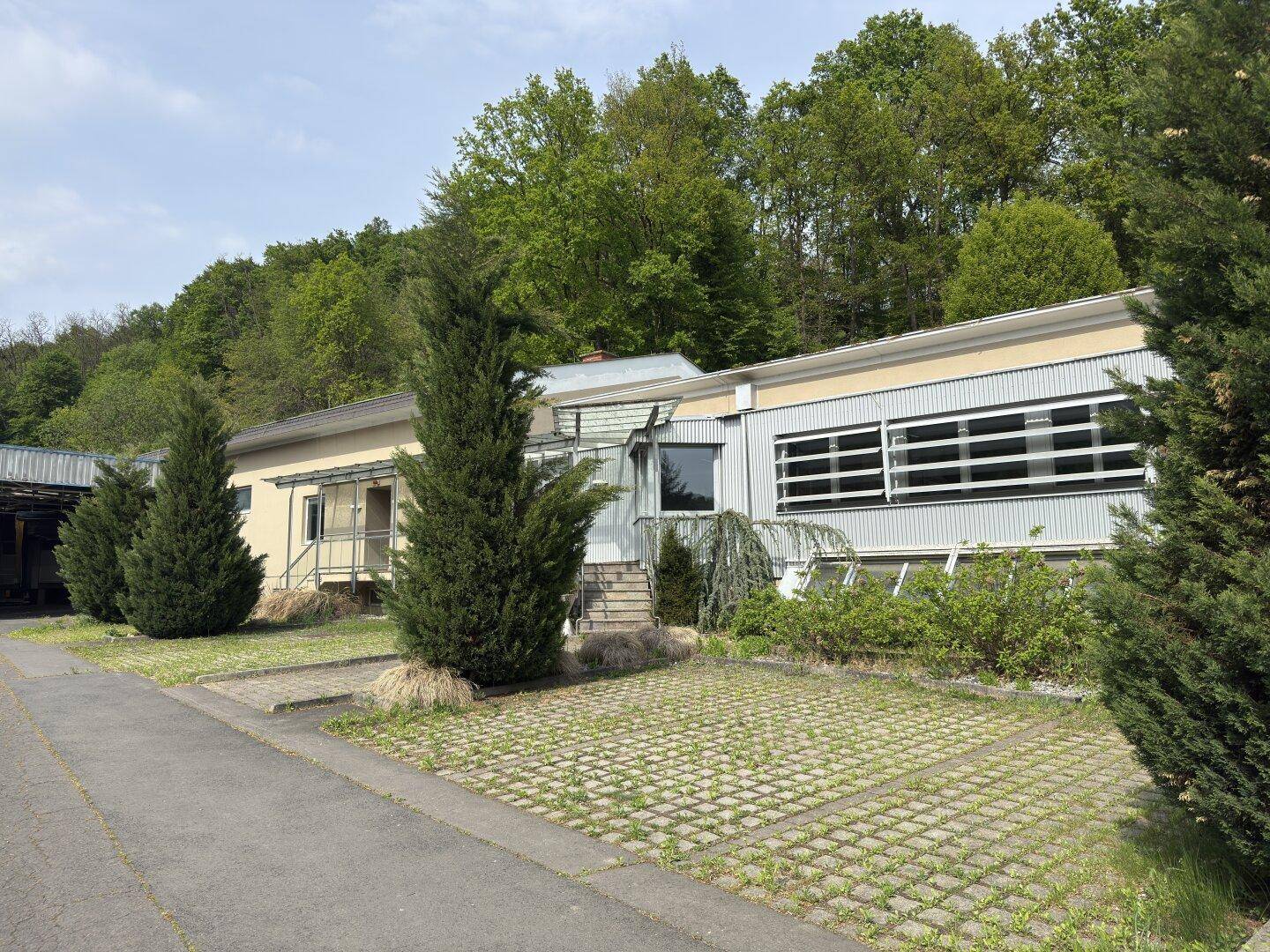Außenansicht eines Geschäftsgebäudes mit Parkplätzen und umgebender grüner Landschaft.