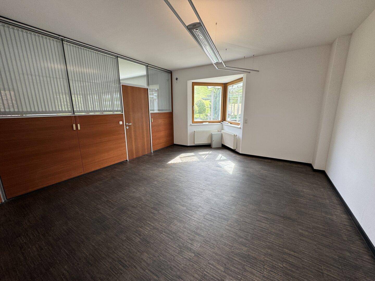 Büro mit Holzwänden und einem Erkerfenster, das eine helle und funktionale Arbeitsfläche bietet.