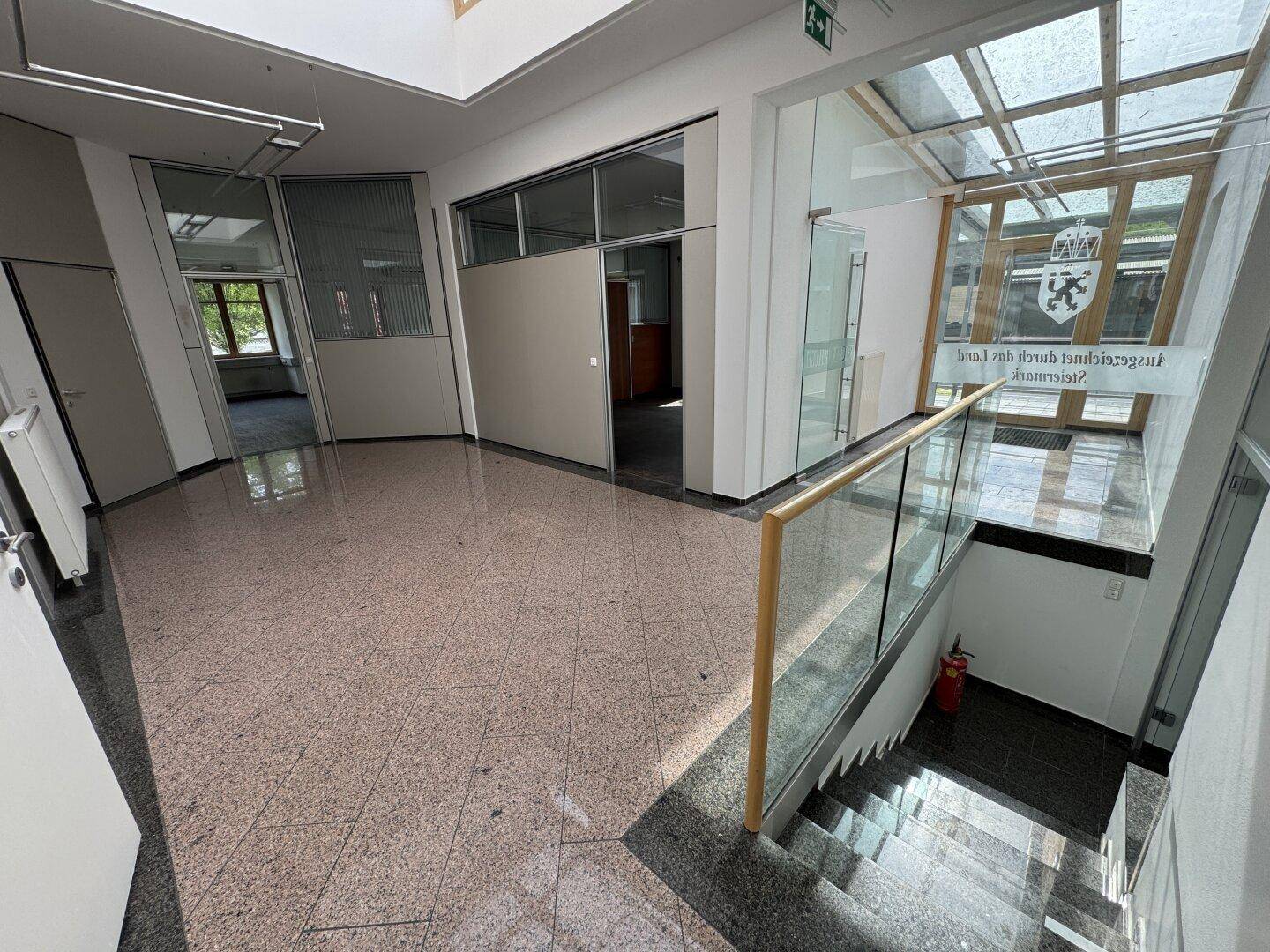 Heller Eingangsbereich mit Granitboden, Glasgeländer und Treppe, die zu weiteren Etagen führt.