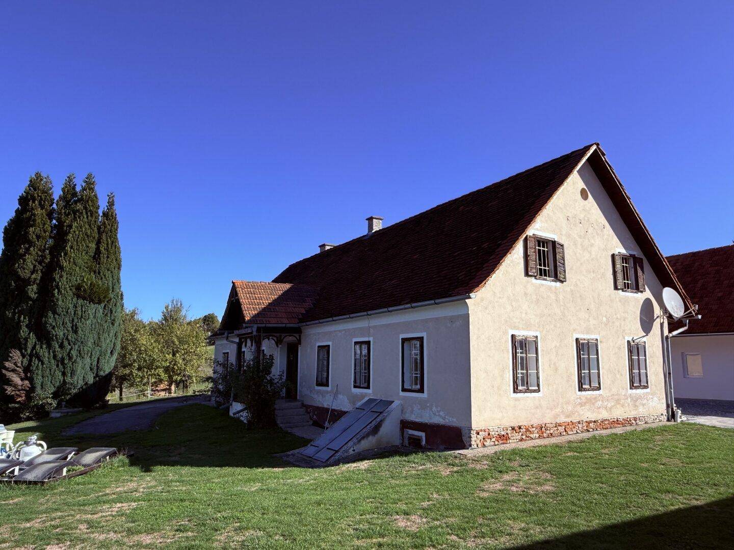 Traditionelles Landhaus mit Satteldach, Holzfensterläden und umgebender Grünfläche.