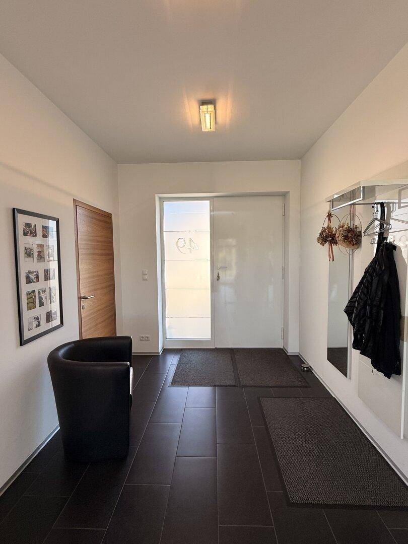 Heller Eingangsbereich mit dunklen Fliesen, Garderobe und einem modernen Sessel.