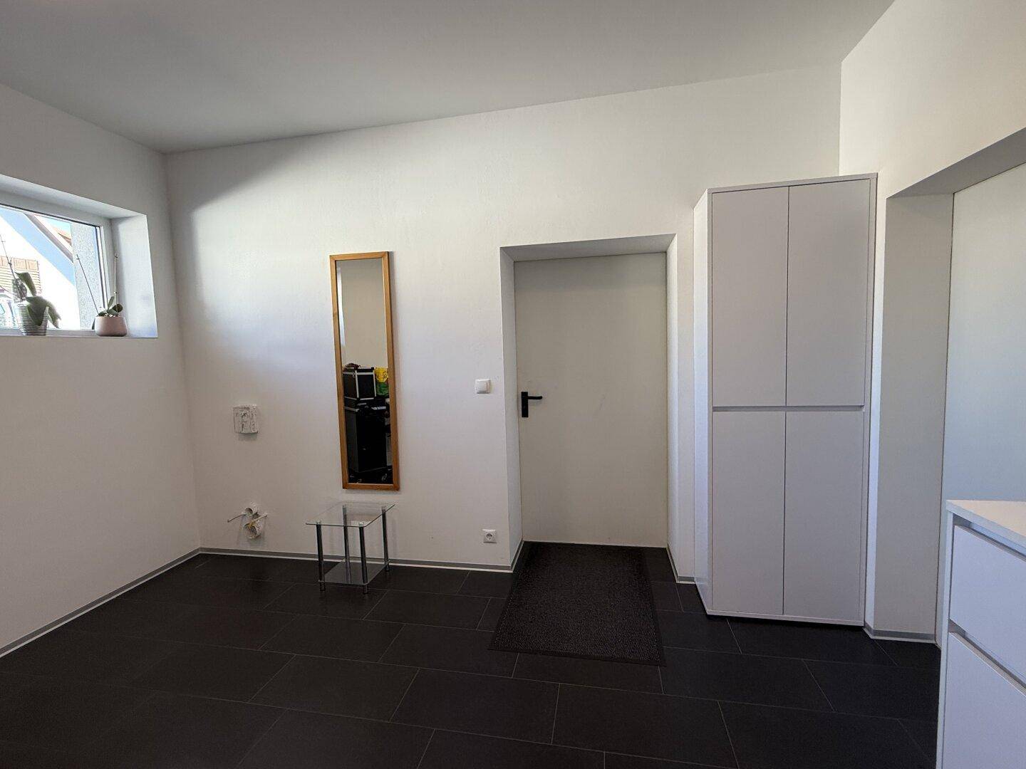Schlichter Flur mit weißen Wänden, dunklen Fliesen und einem schmalen Fenster.