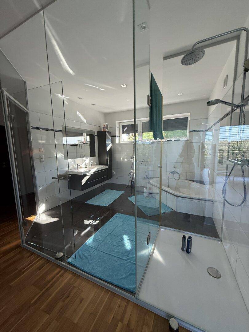 Modernes Badezimmer mit großer Glasdusche, Eckbadewanne und Holzboden.