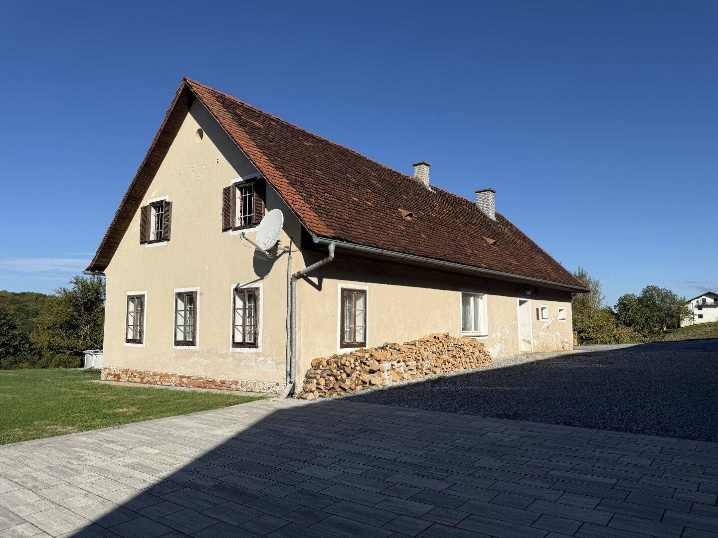 Traditionelles Gebäude mit Satteldach, Holzstapel und gepflastertem Vorplatz.