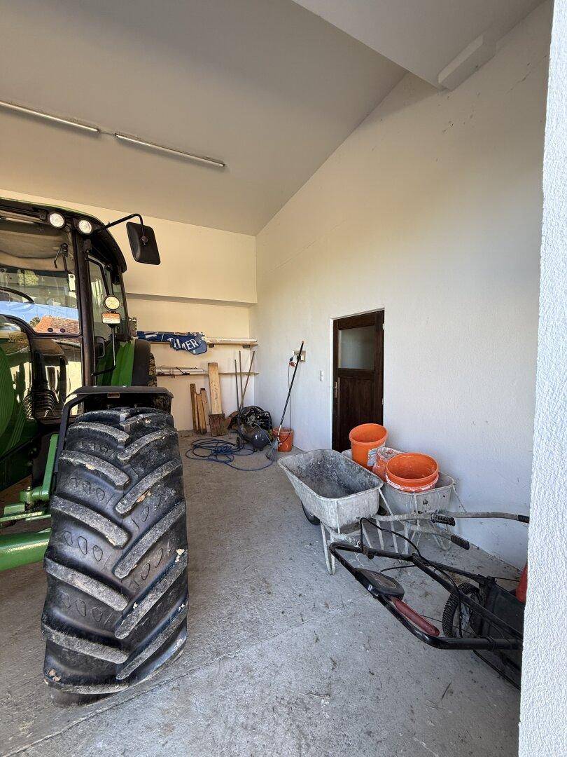 Geräumige Garage mit Betonboden, einem Traktor und verschiedenen Werkzeugen und Geräten.