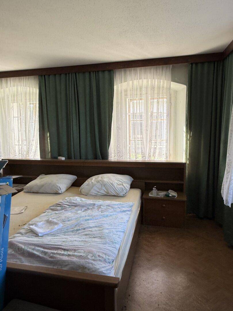 Schlafzimmer mit Doppelbett, Holzvertäfelung und zwei Fenstern mit grünen Vorhängen.