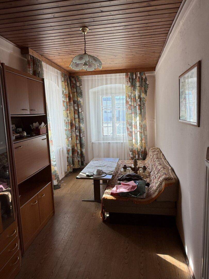 Gemütliches Zimmer mit Holzbalkendecke, Parkettboden und einem Fenster mit Vorhängen.