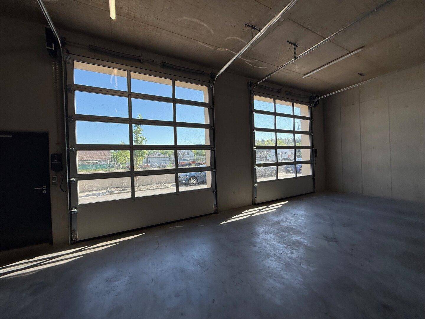 Geräumiger Innenbereich einer Garage mit zwei großen, verglasten Toren, die viel Tageslicht hereinlassen.