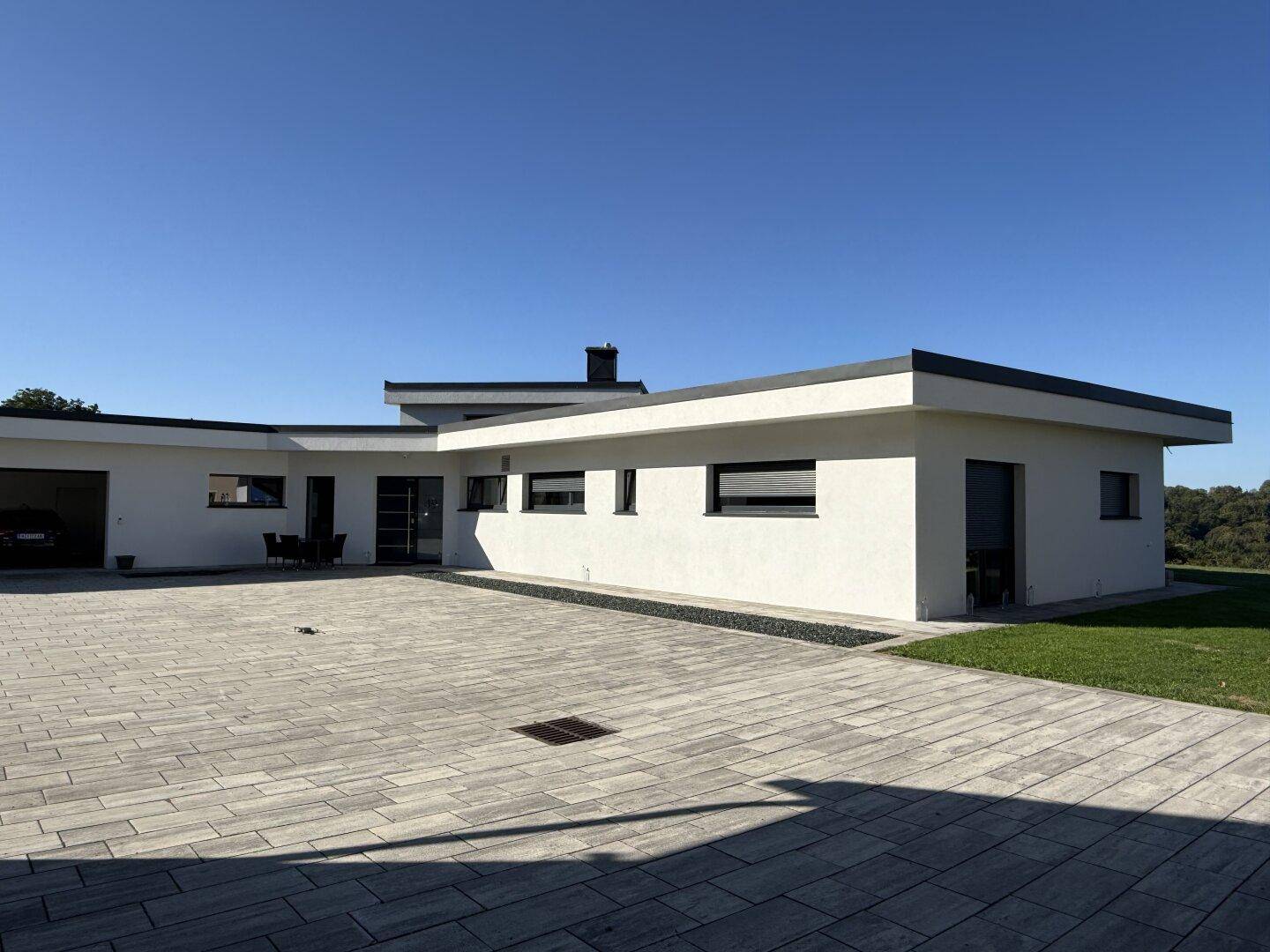 Modernes Gebäude mit flachem Dach und großzügigem, gepflastertem Vorplatz.