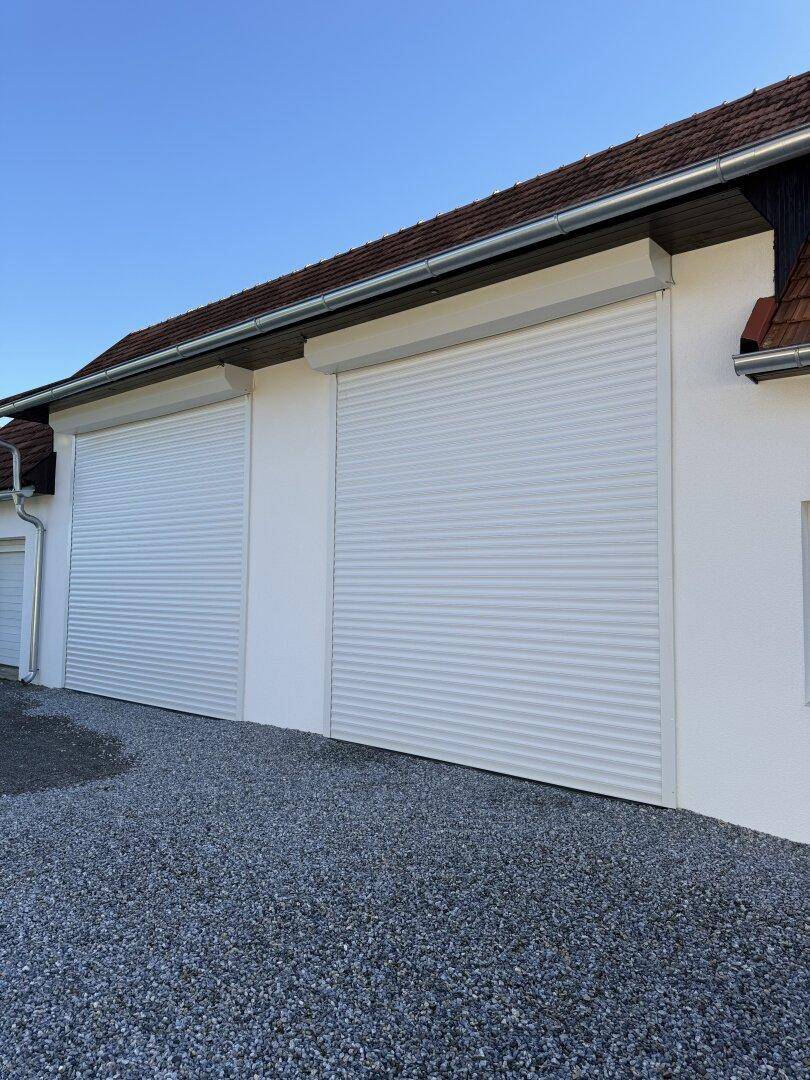 Weiße Fassade eines Gebäudes mit zwei großen Rolltoren, wahrscheinlich für Garagenzugänge.