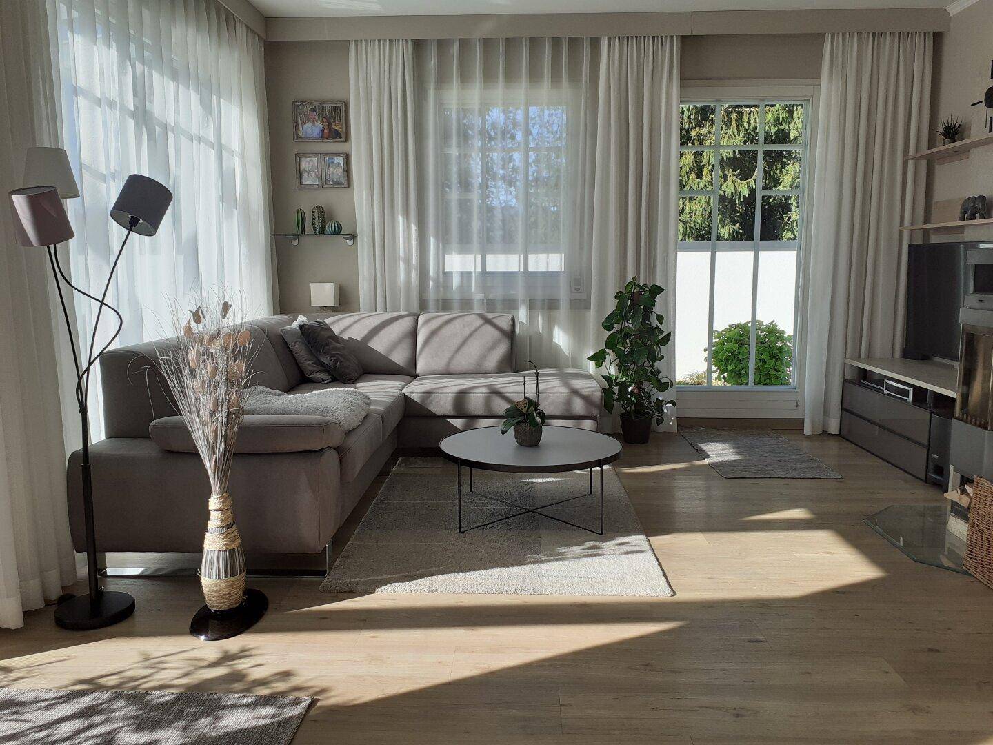 Helles Wohnzimmer mit großem Ecksofa, Holzboden und bodentiefen Fenstern.