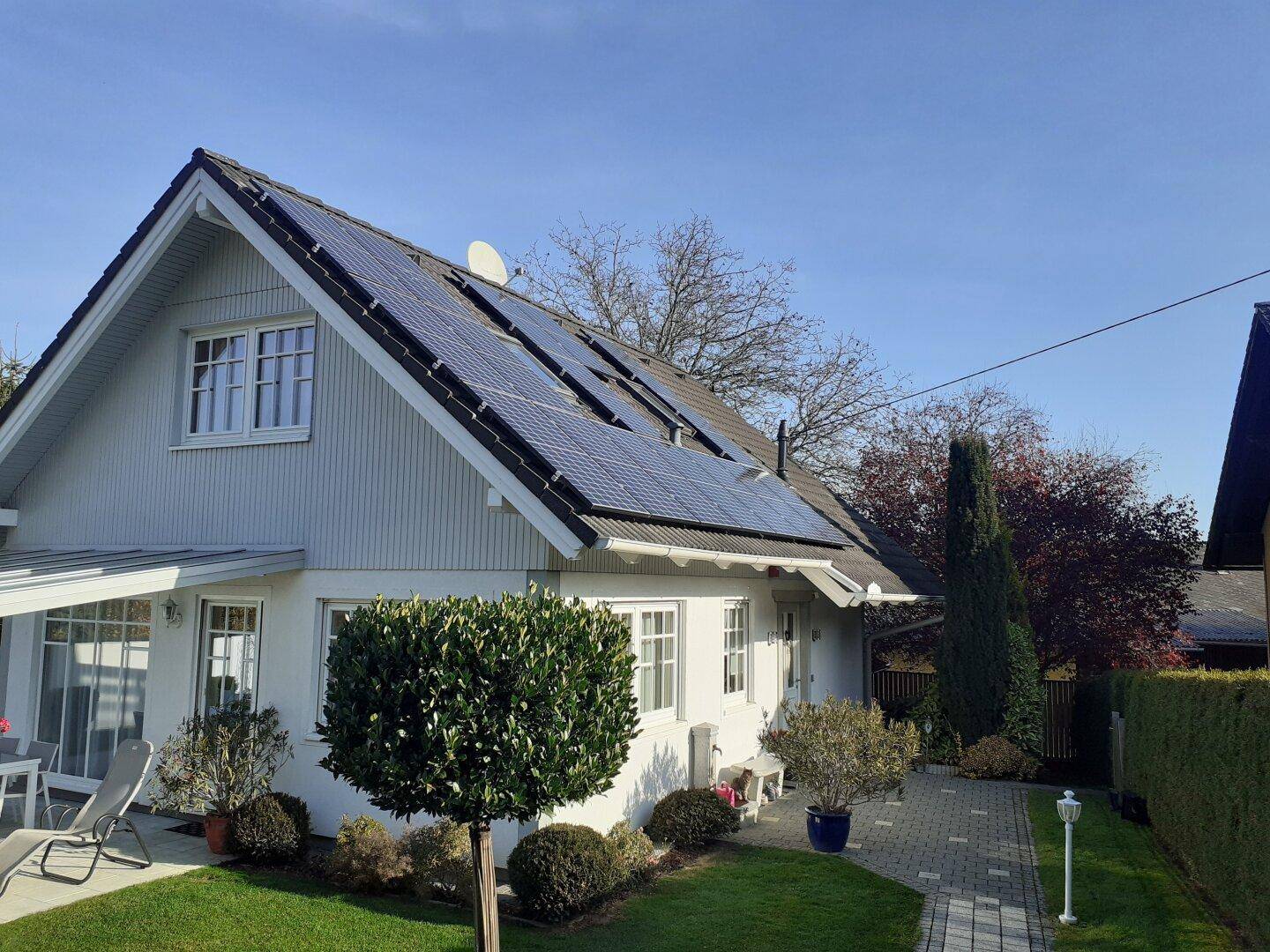 Weißes Einfamilienhaus mit Satteldach und Photovoltaikanlage auf dem Dach.