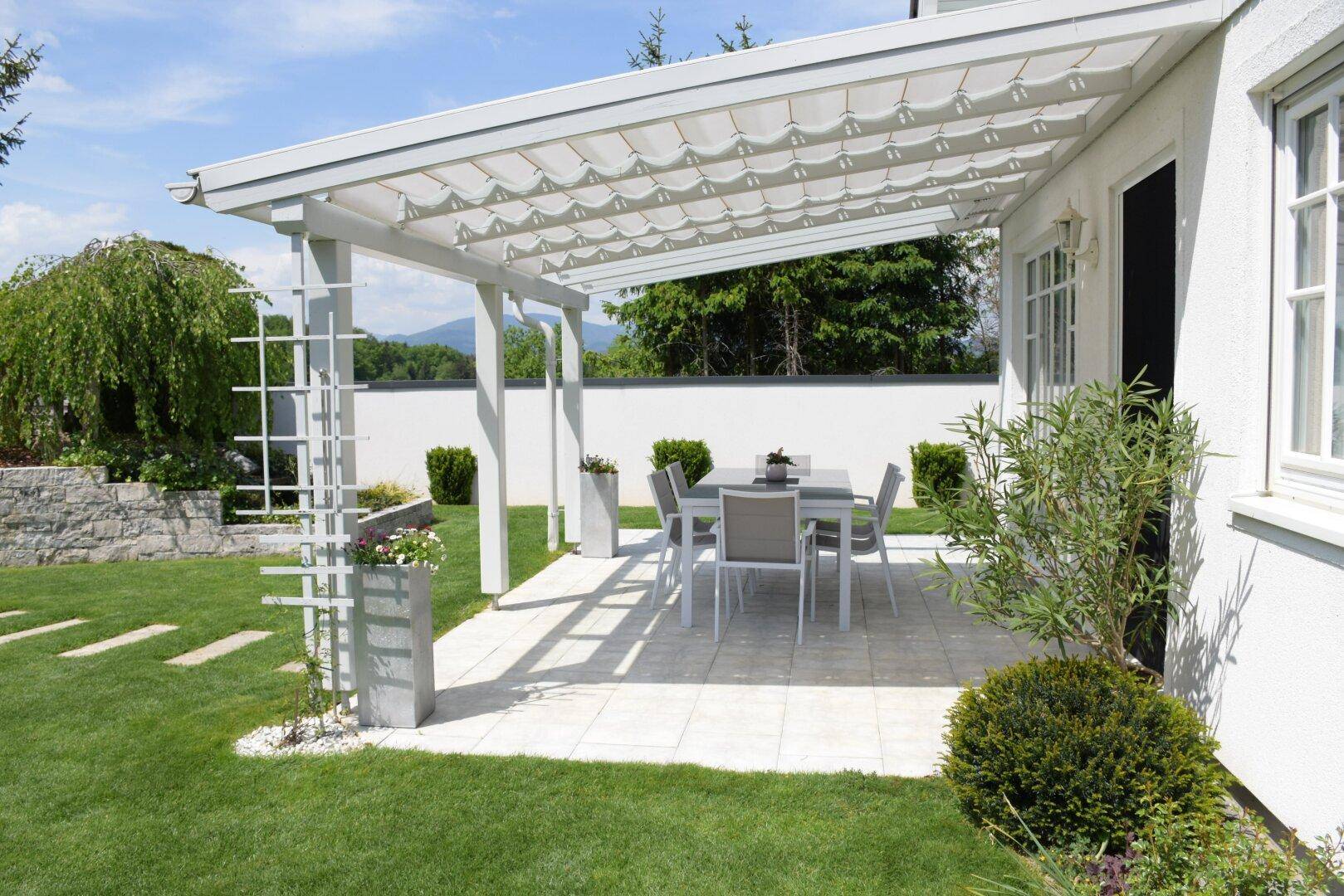 Sonniger Terrassenbereich mit Pergola, Esstisch und Blick auf den gepflegten Garten.