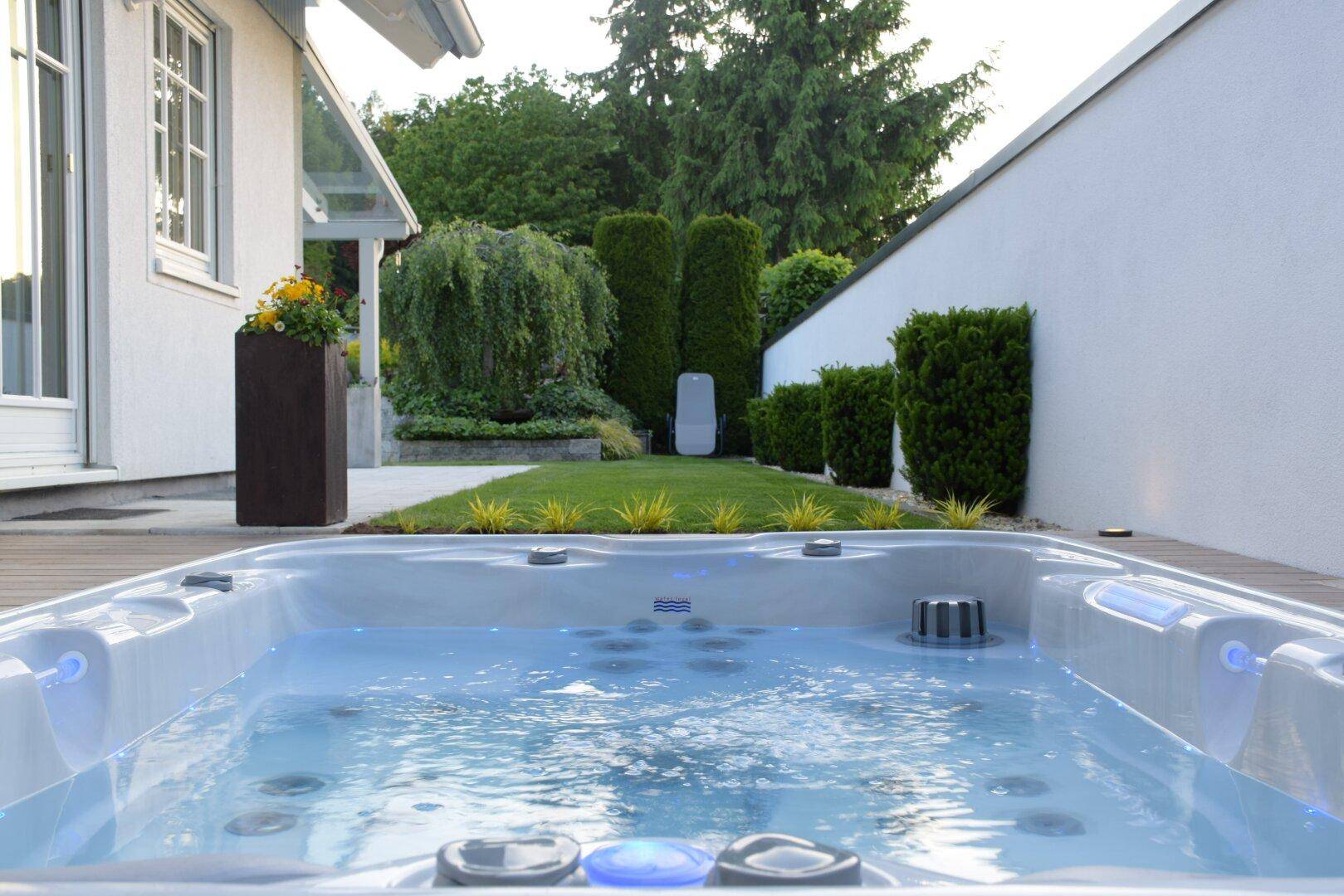Moderner Whirlpool im Gartenbereich mit Holzdeck und umgebender Grünfläche.