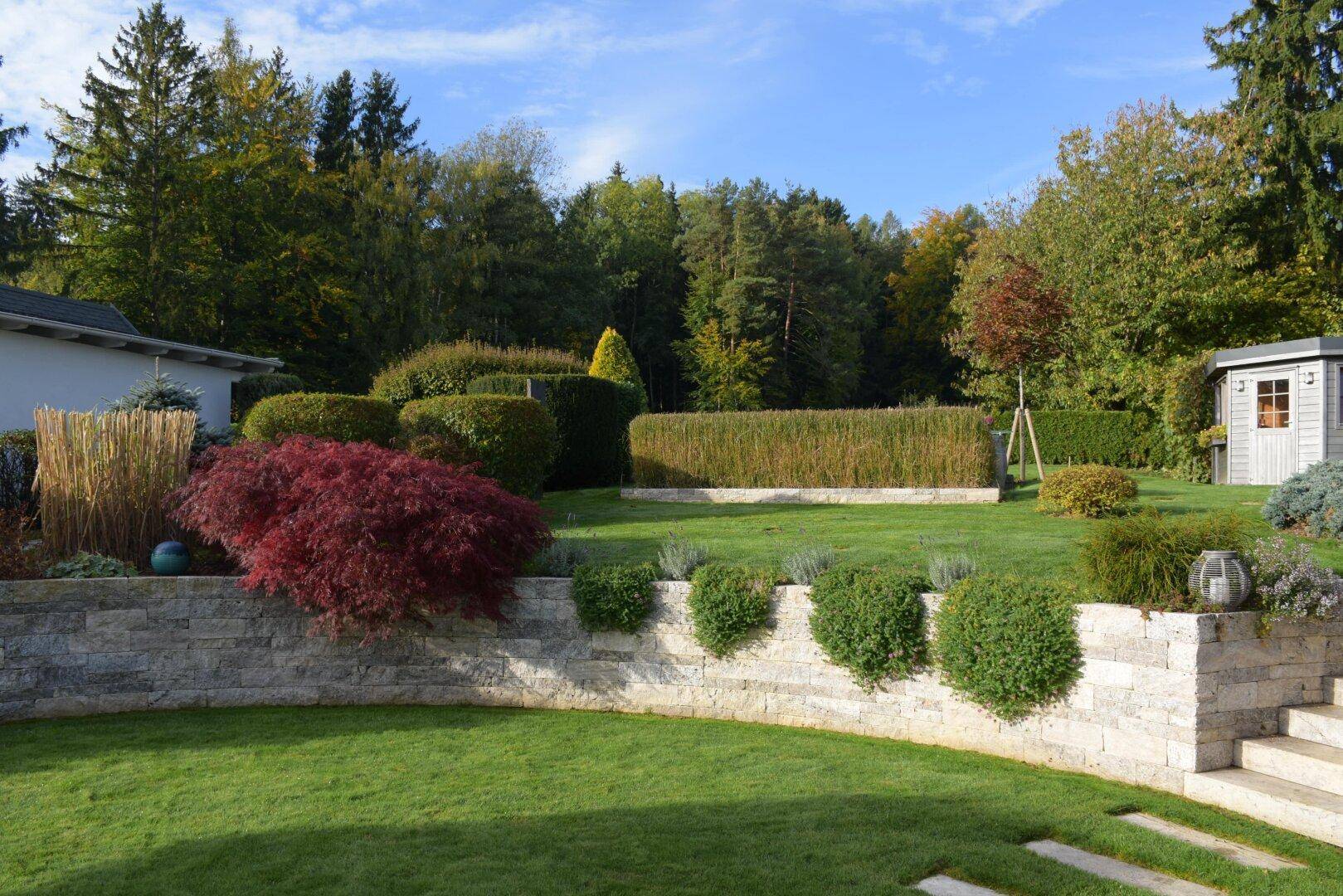 Großer, gepflegter Garten mit Steinmauern, verschiedenen Pflanzen und Bäumen.