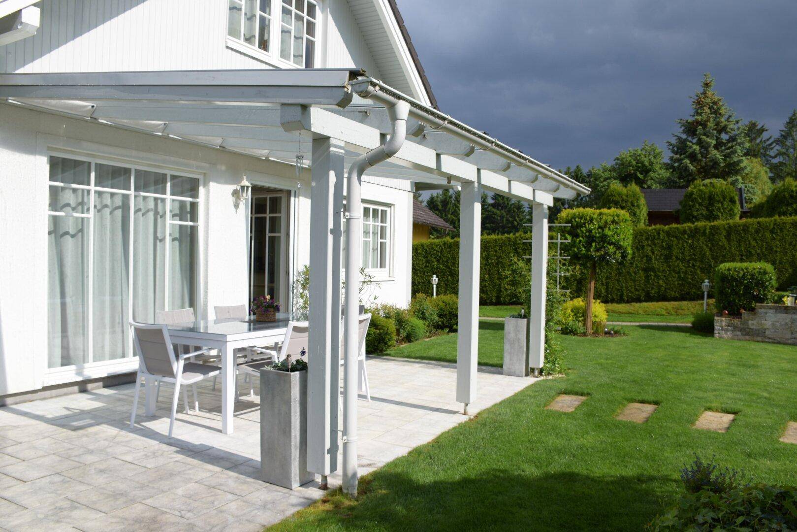Überdachte Terrasse mit Esstisch und Stühlen, umgeben von einem grünen Garten.