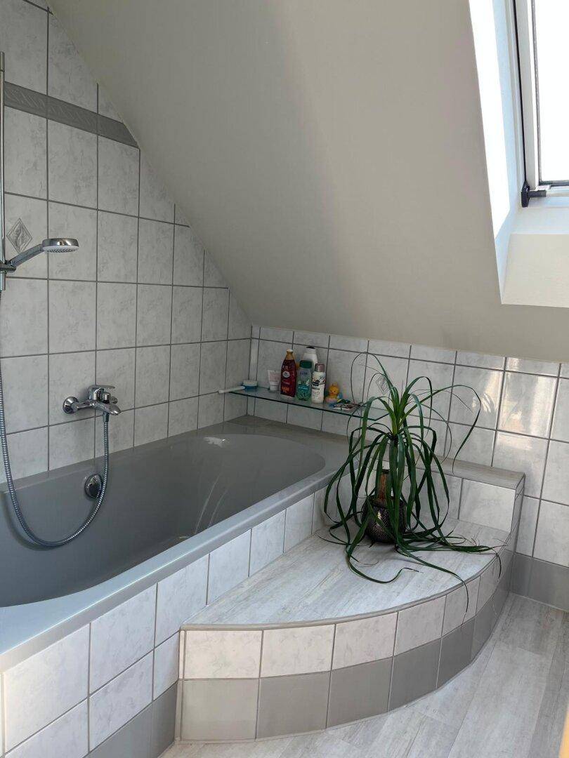 Badezimmer im Dachgeschoss mit Badewanne, hellen Fliesen und Dachfenster.