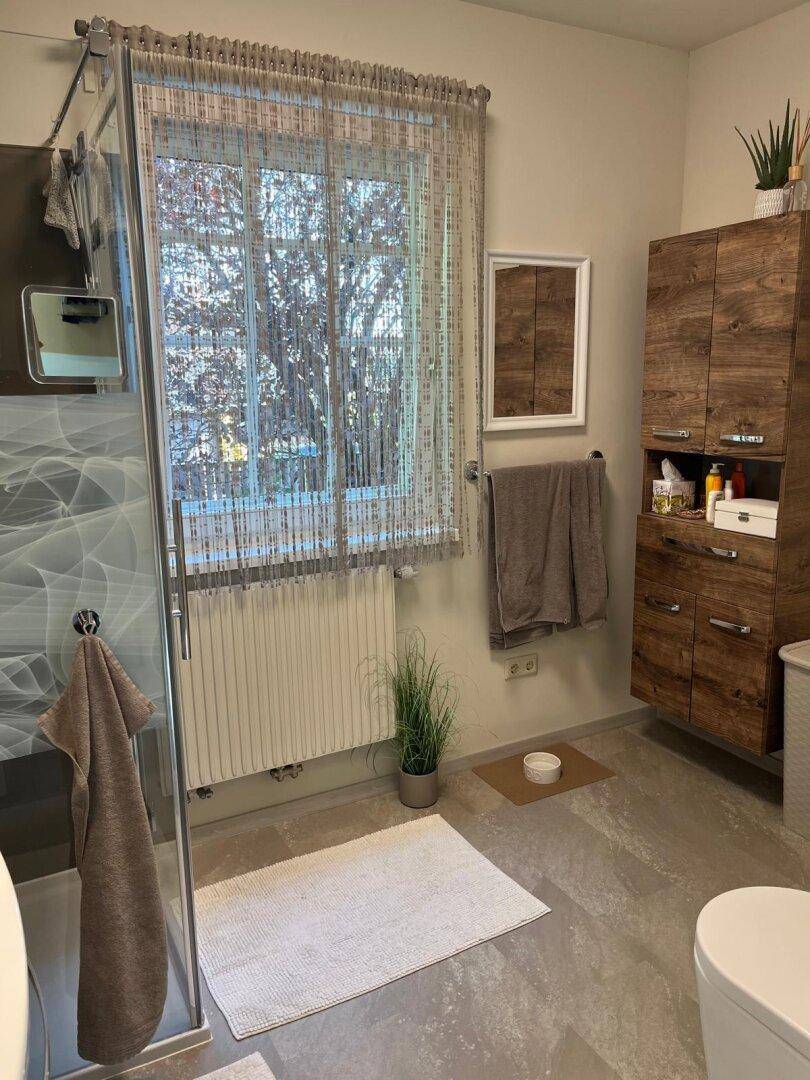 Modernes Badezimmer mit Duschkabine, Holzschrank und Fenster für Tageslicht.