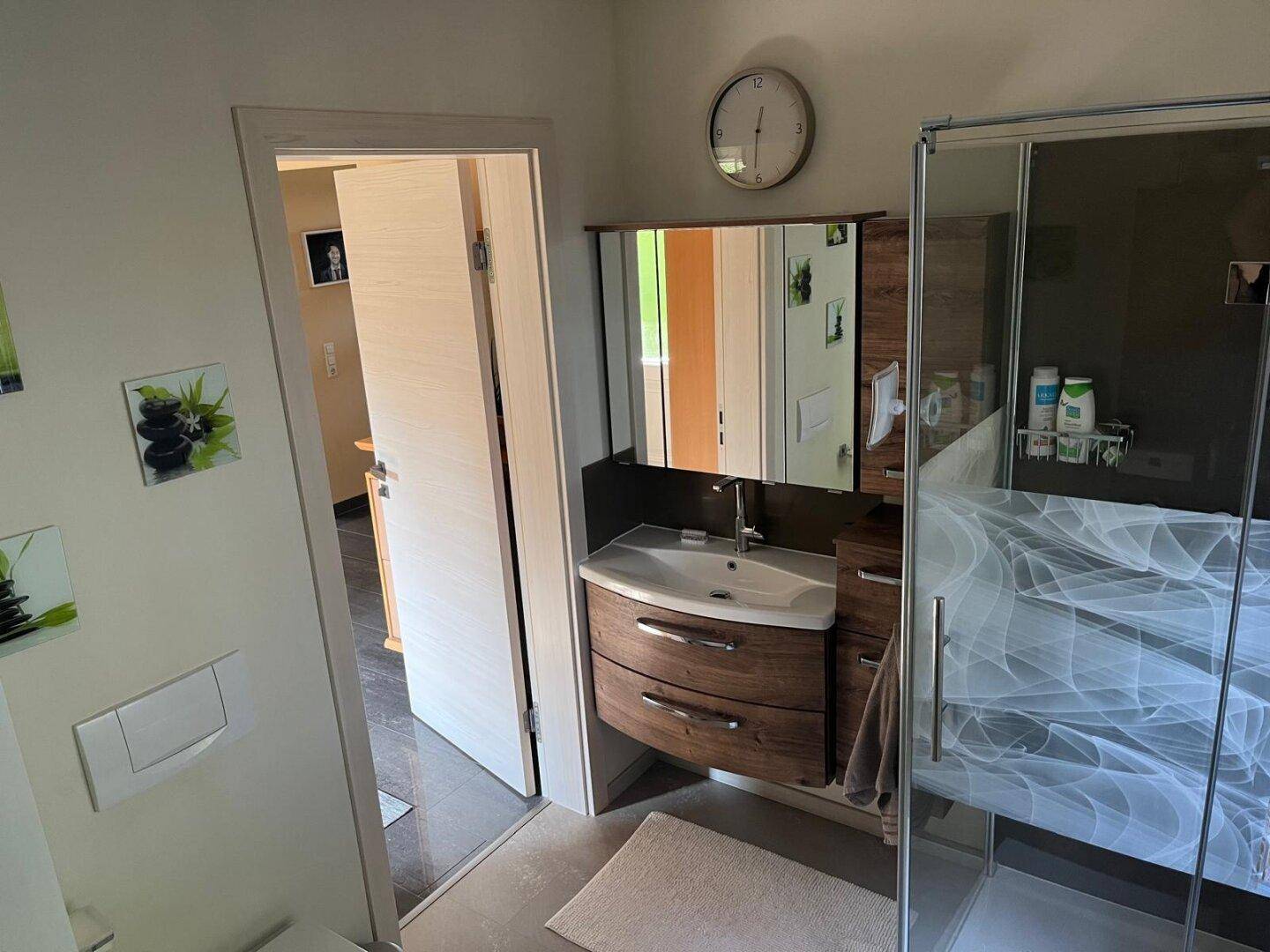 Badezimmer mit modernem Waschtisch, Spiegelschrank und Duschbereich.