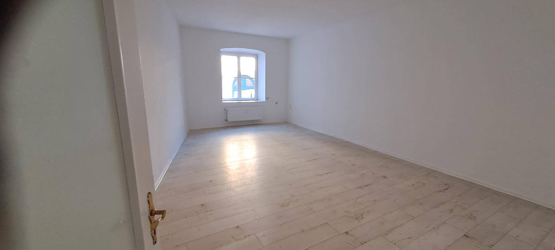 Geräumiger, heller Raum mit hellem Laminatboden und einem Fenster für natürliches Licht.