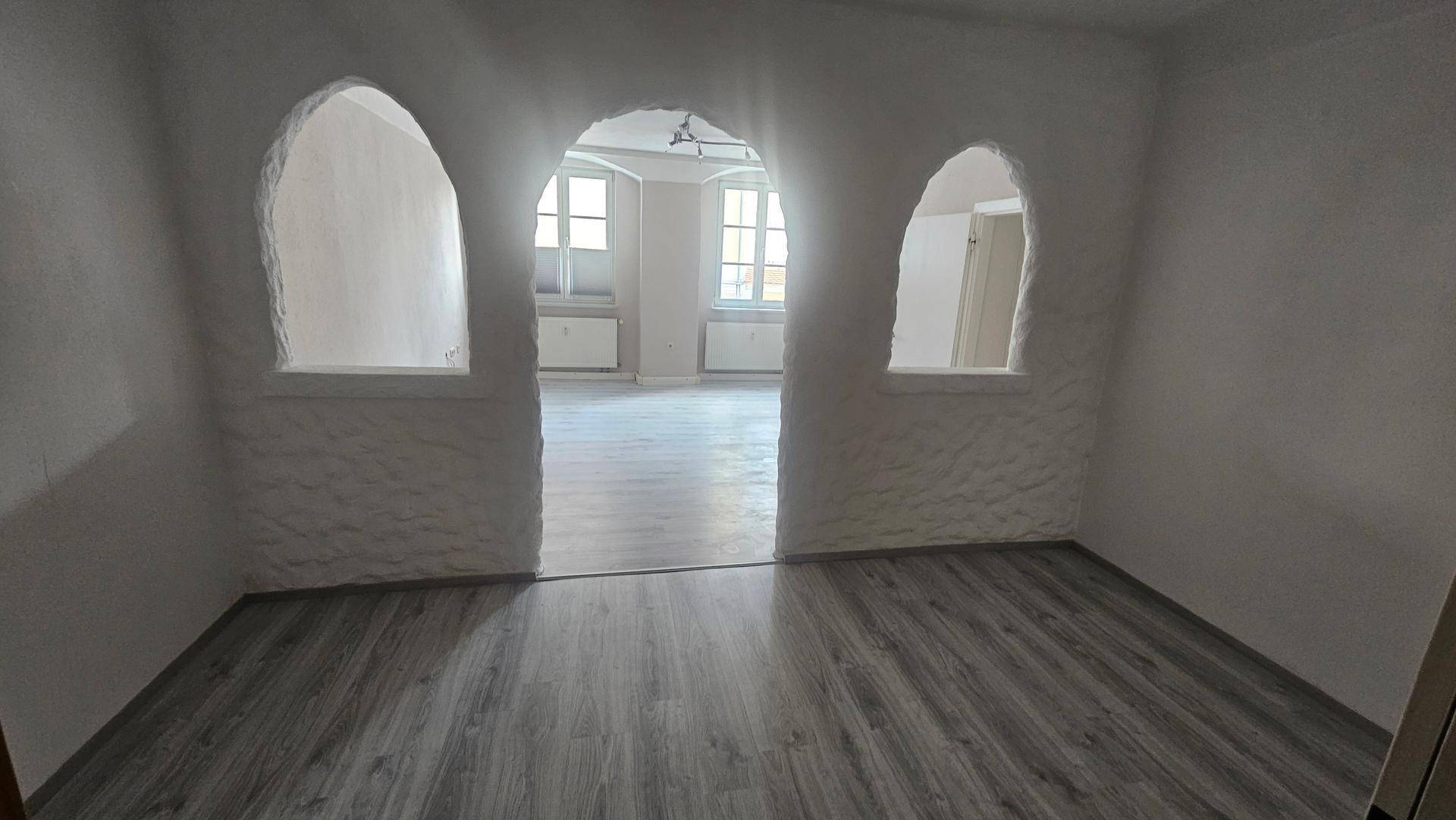 Unmöbliertes Zimmer mit dekorativen Rundbögen, die den Blick in einen weiteren Raum freigeben.