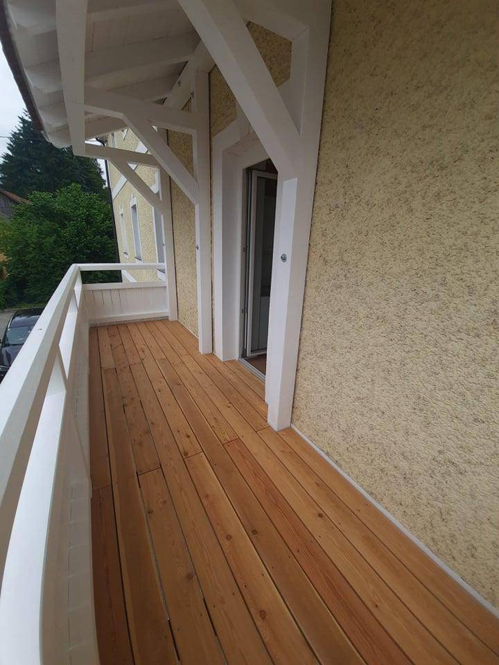 Neuer Holzbalkon mit weißem Geländer und Blick auf die Umgebung.